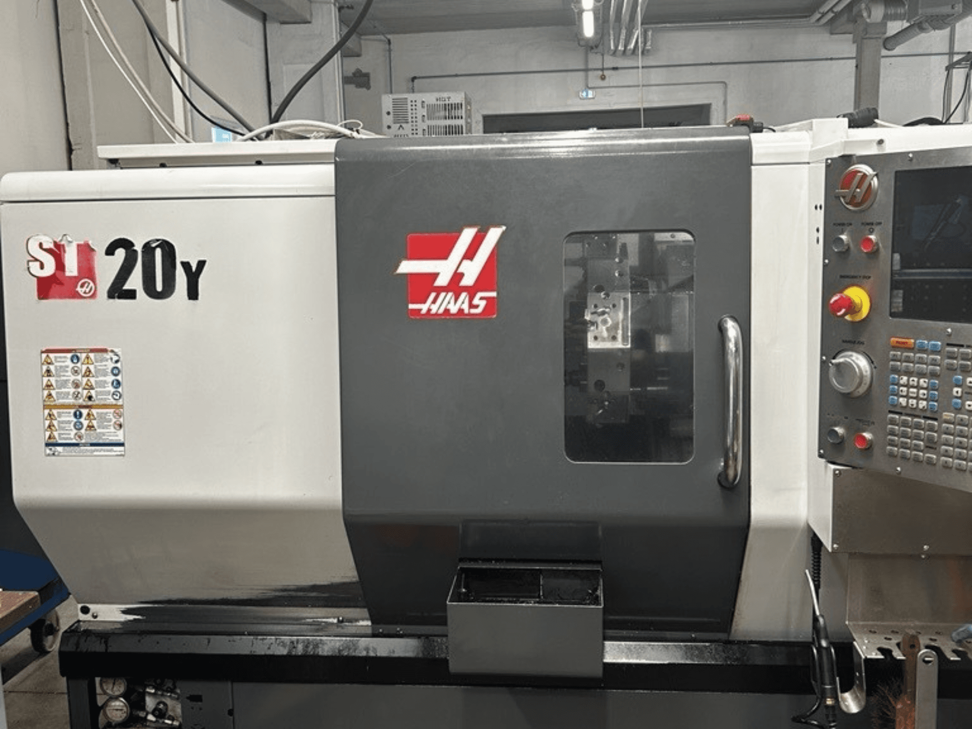 Tokarka CNC Haas ST-20Y, widok z przodu, z panelem sterowania, etykietami bezpieczeństwa i oknem roboczym.