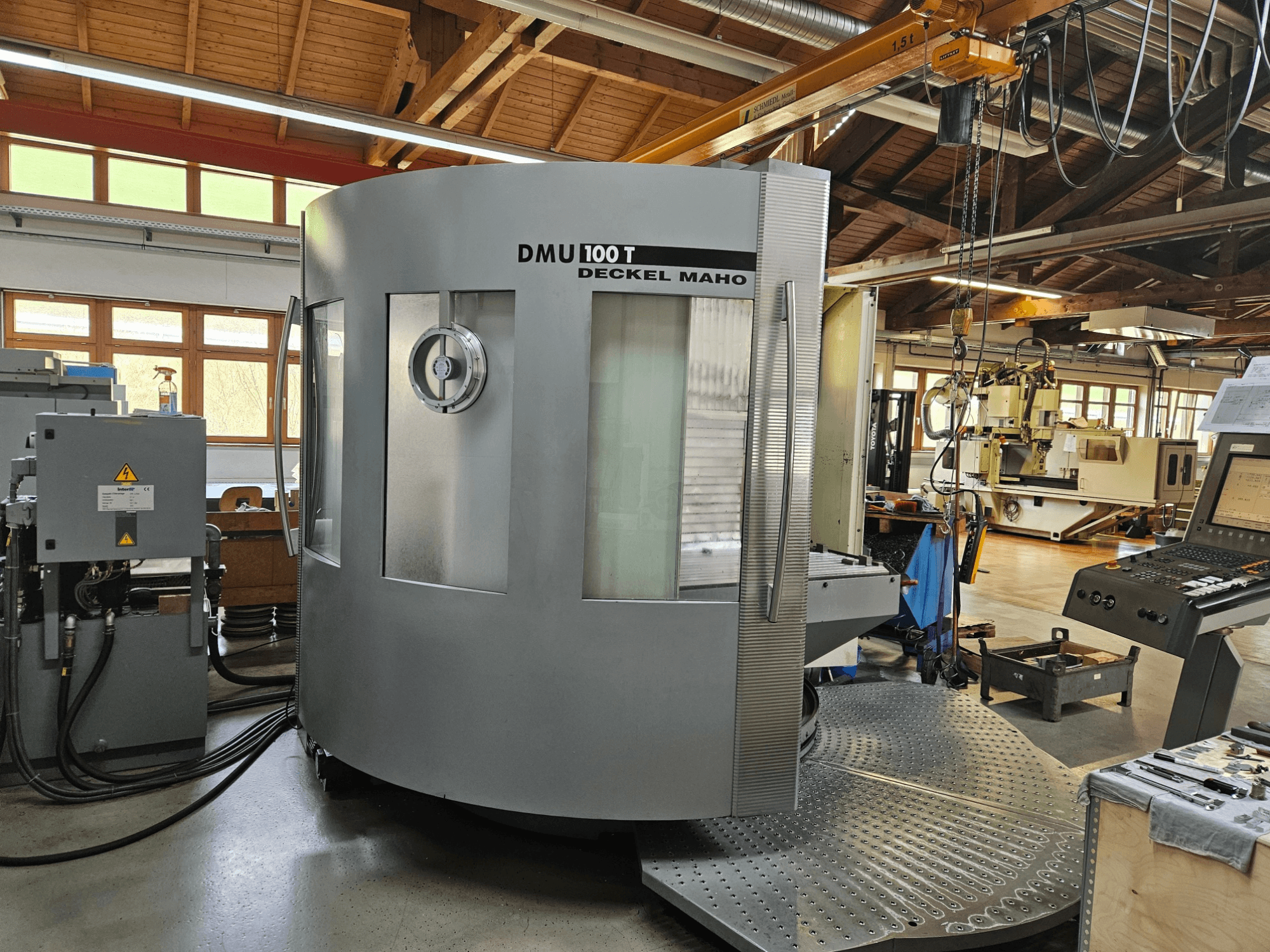 Maszyna CNC DMU 100 T Deckel Maho widziana od przodu, z dużą okrągłą podstawą, panelem sterowania i szklaną obudową.