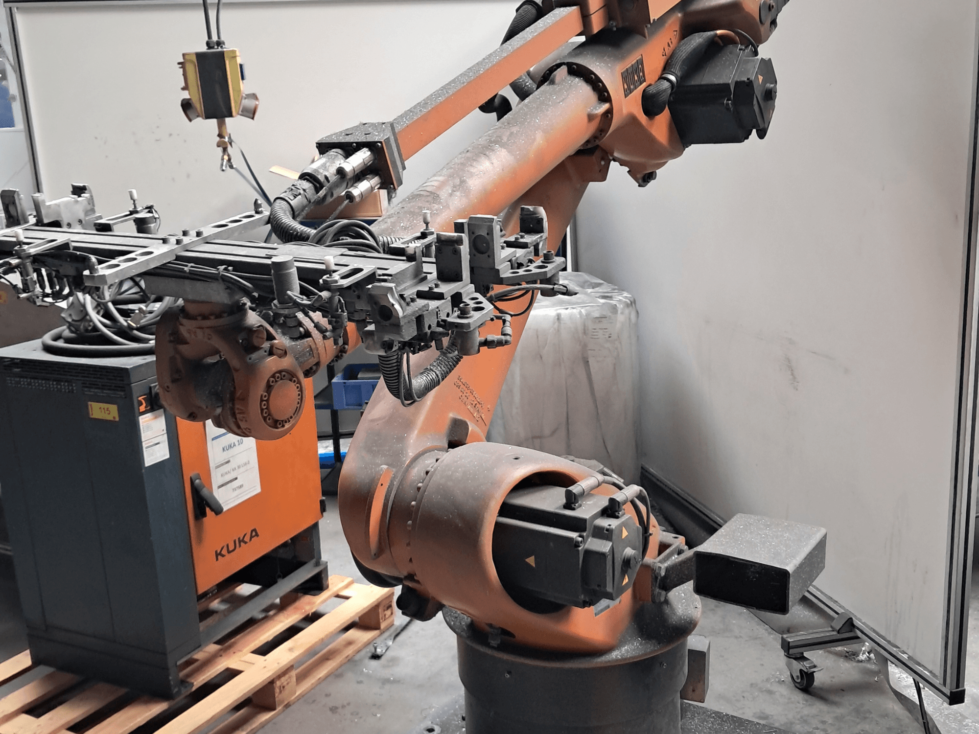 Ramię robota KUKA KR 30L16-2 widziane z boku, wyposażone w skomplikowany efektor końcowy i kable sterujące, umieszczone obok skrzynki sterowniczej KUKA.