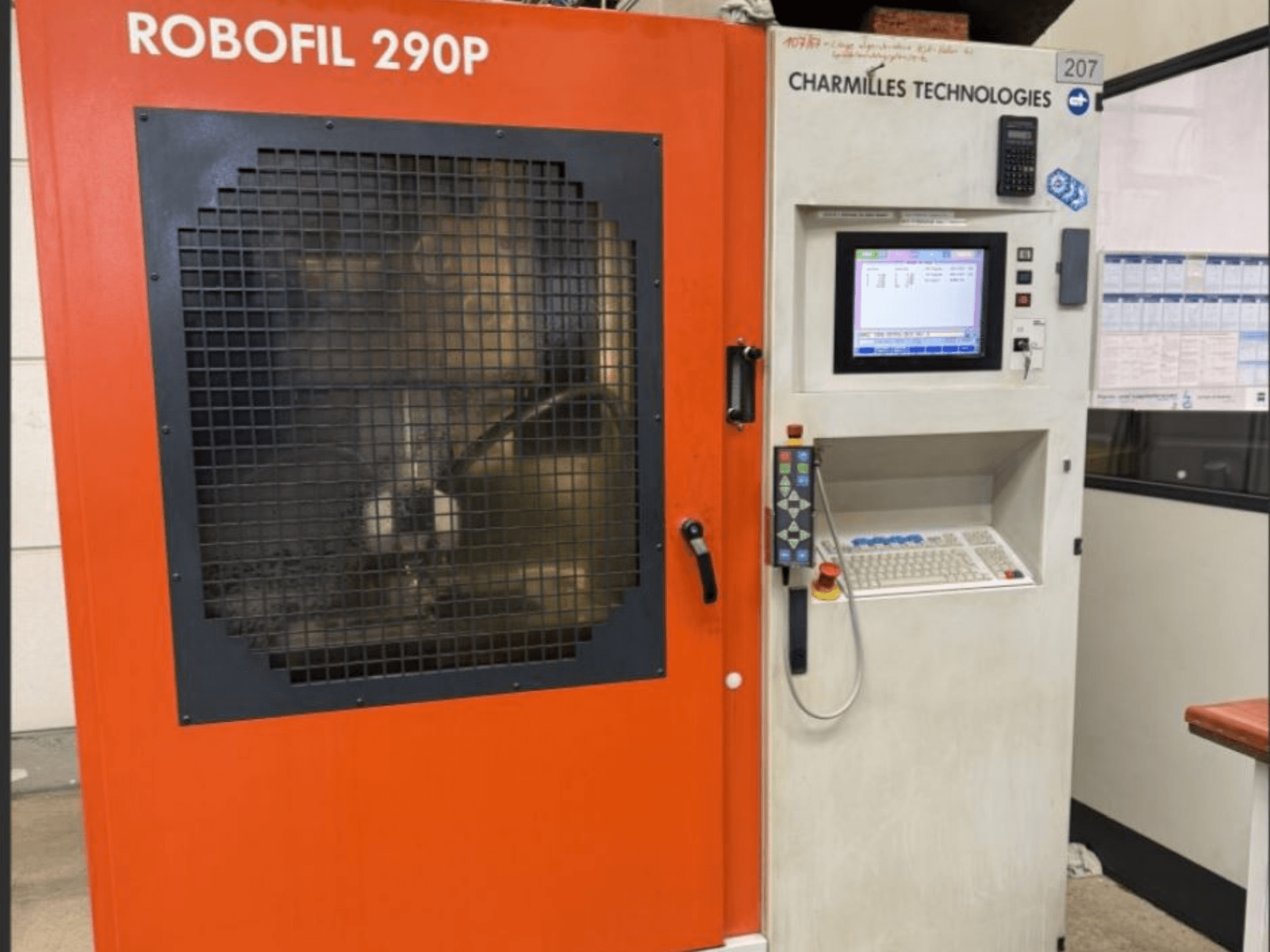 Widok z przodu elektrodrążarki drutowej Robofil 290P firmy CHARMILLES TECHNOLOGIES z panelem sterowania i obszarem roboczym zabezpieczonym siatką.