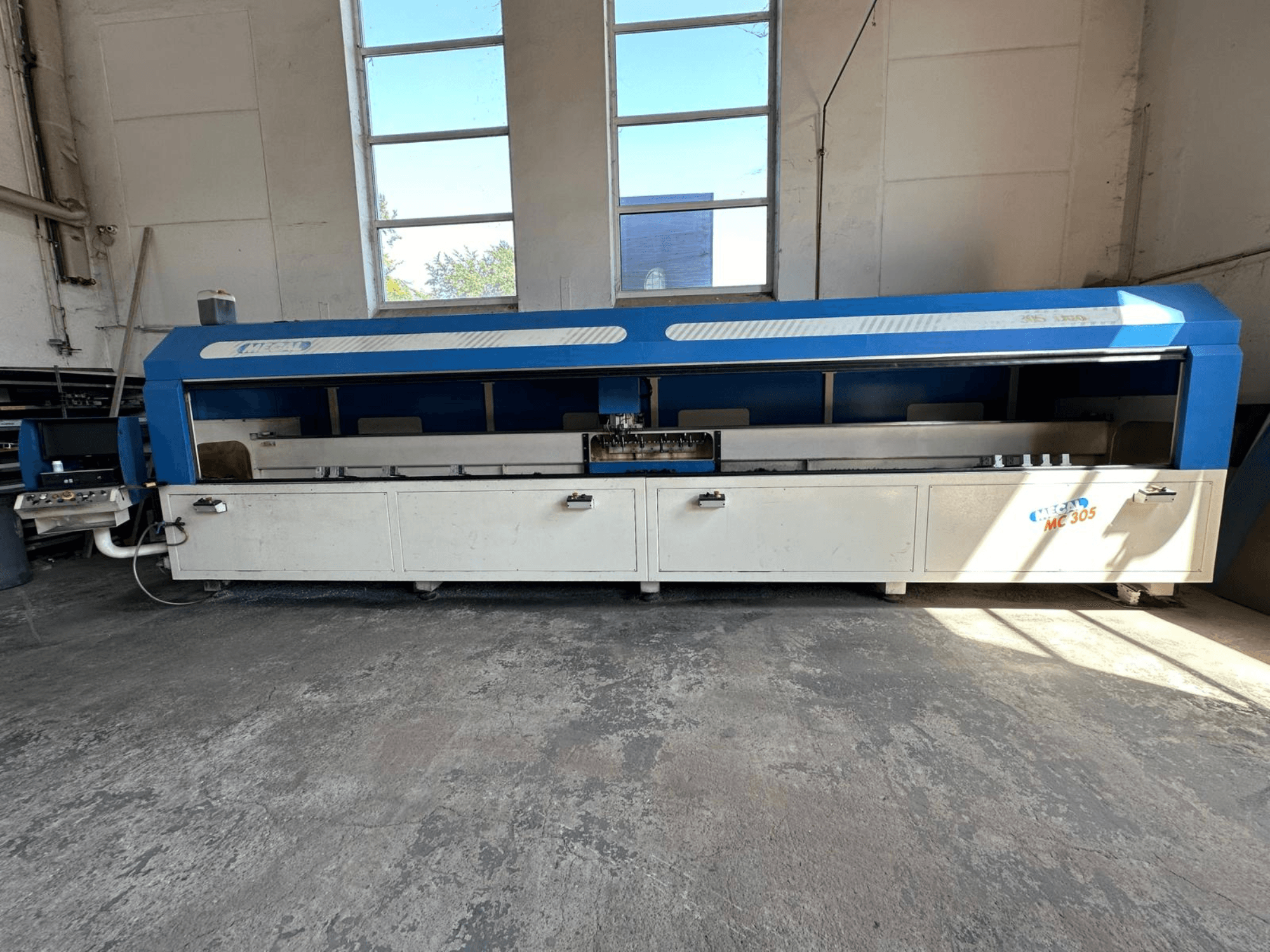 Widok z przodu pionowego centrum obróbczego MECAL MC 305 z niebiesko-białym designem, widocznym stołem roboczym i panelem sterowania.