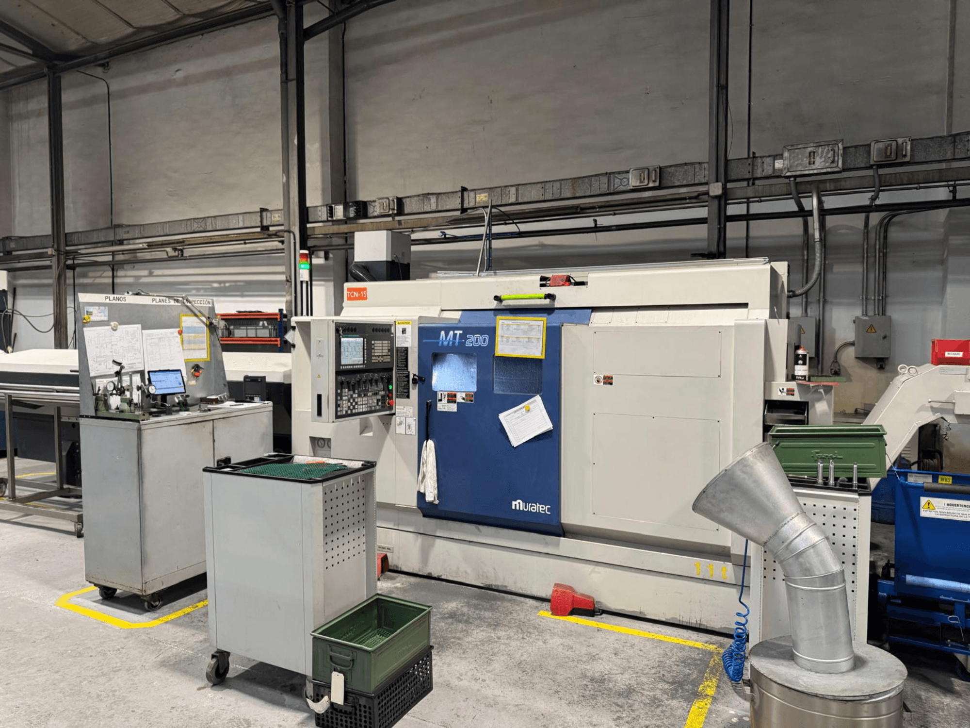 Tokarka wielowrzecionowa Muratec MT200 w warunkach fabrycznych, widziana od przodu, z panelem sterowania i otaczającym wyposażeniem.