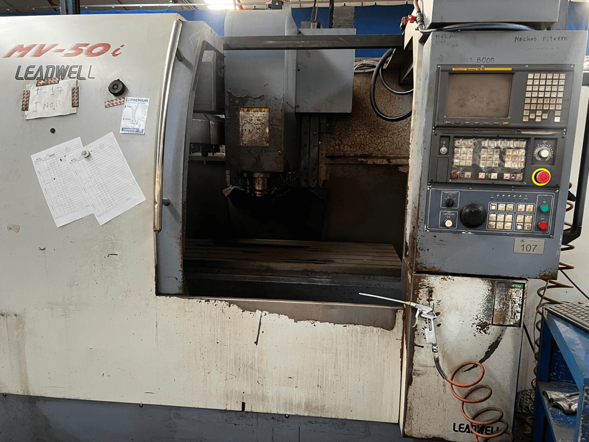 Pionowe centrum obróbcze Leadwell MV-50i, widok z przodu, przedstawiający panel sterowania, obszar wrzeciona oraz stół roboczy z widocznymi śladami zużycia.