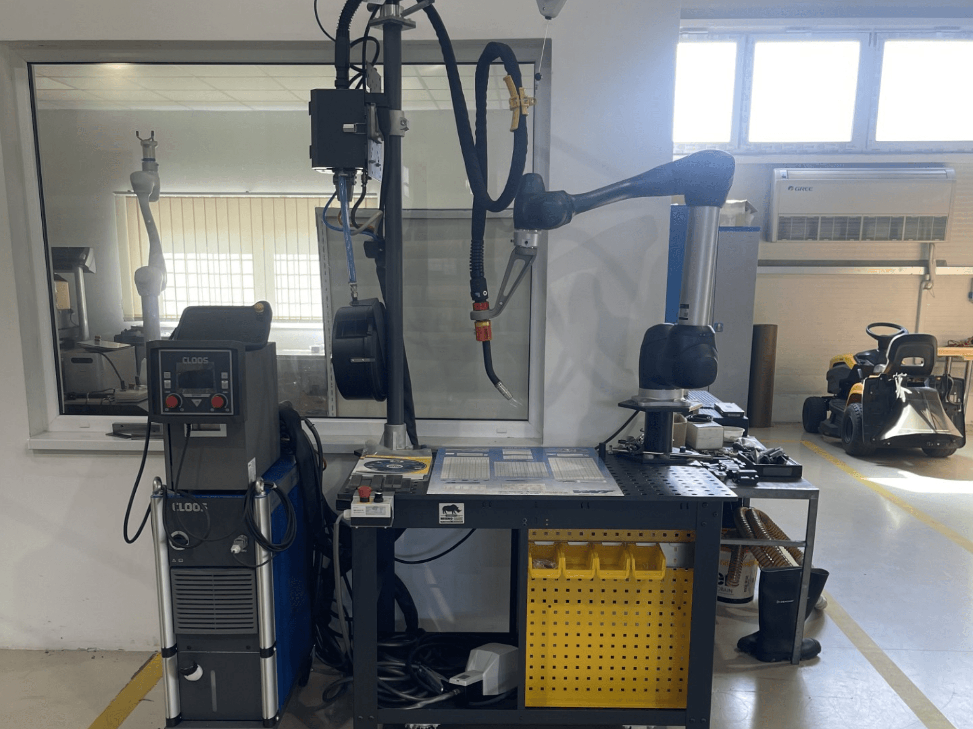 Robot współpracujący DOOSAN M1013 w warsztacie, widok z boku z urządzeniami spawalniczymi i narzędziami na stole warsztatowym.