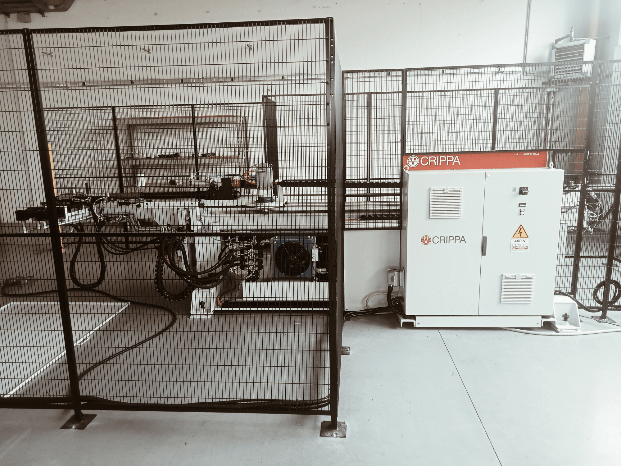 Biała maszyna CRIPPA za klatką bezpieczeństwa, z widocznymi wężami i komponentami, widok z boku, otoczenie przemysłowe.