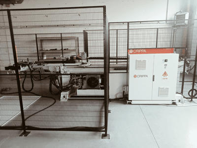 Biała maszyna CRIPPA za klatką bezpieczeństwa, z widocznymi wężami i komponentami, widok z boku, otoczenie przemysłowe.