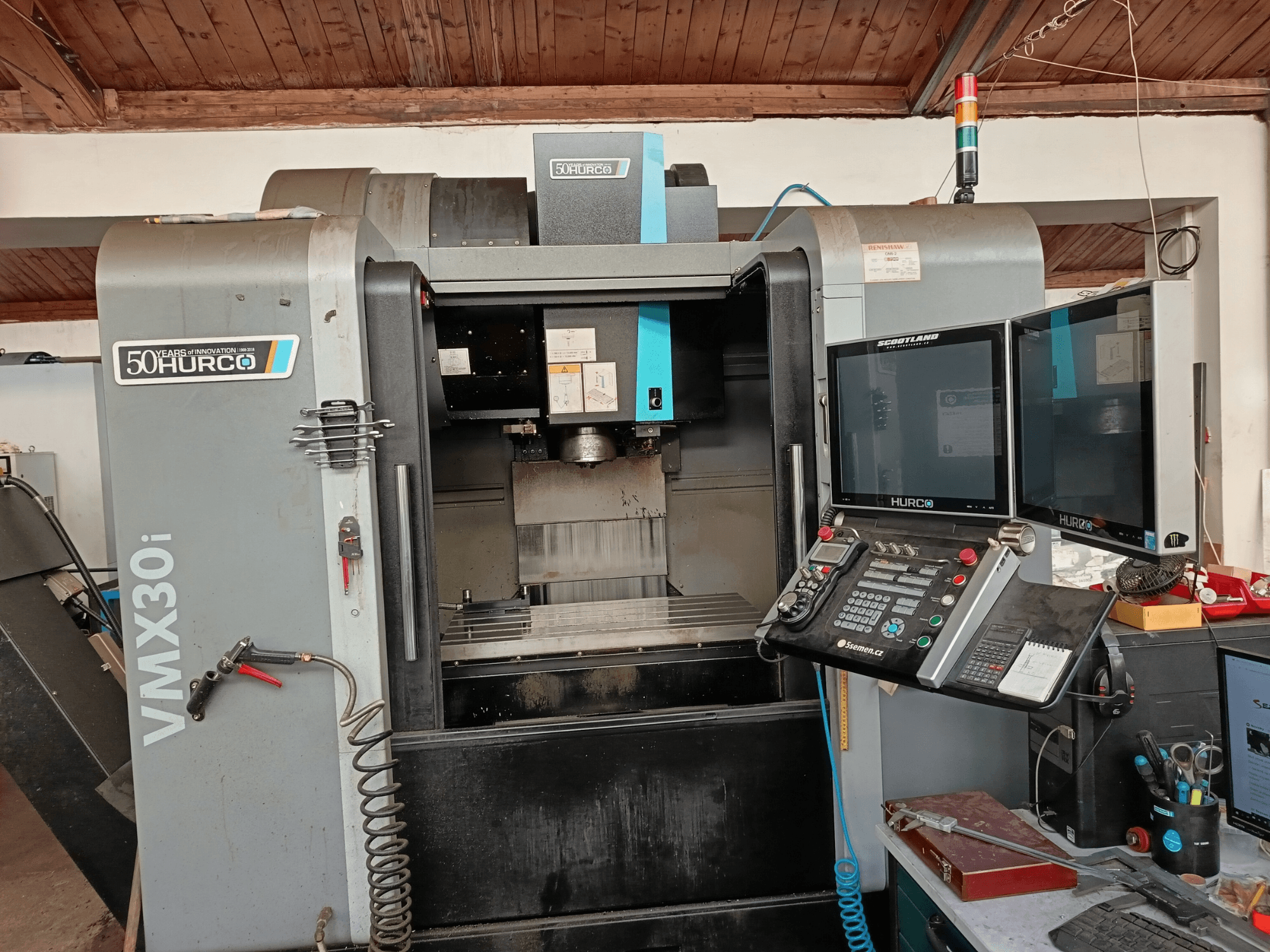 Frezarka CNC Hurco VMX30i w widoku z przodu, z dwoma monitorami, panelem sterowania i podłączonym wężem.