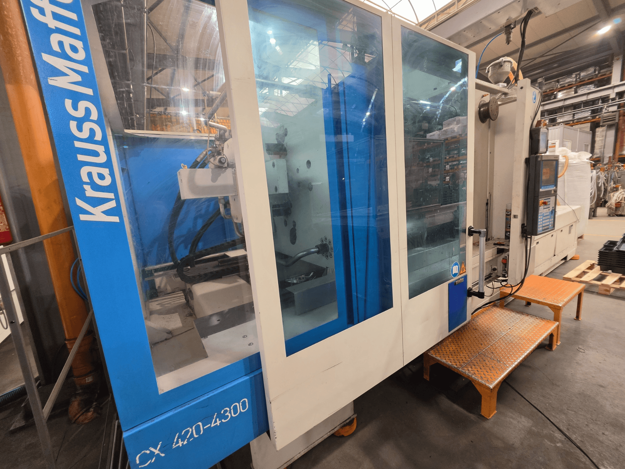 Hydrauliczna wtryskarka Krauss Maffei CX 420-4300, widok z boku, pokazujący panel sterowania i przezroczyste panele.