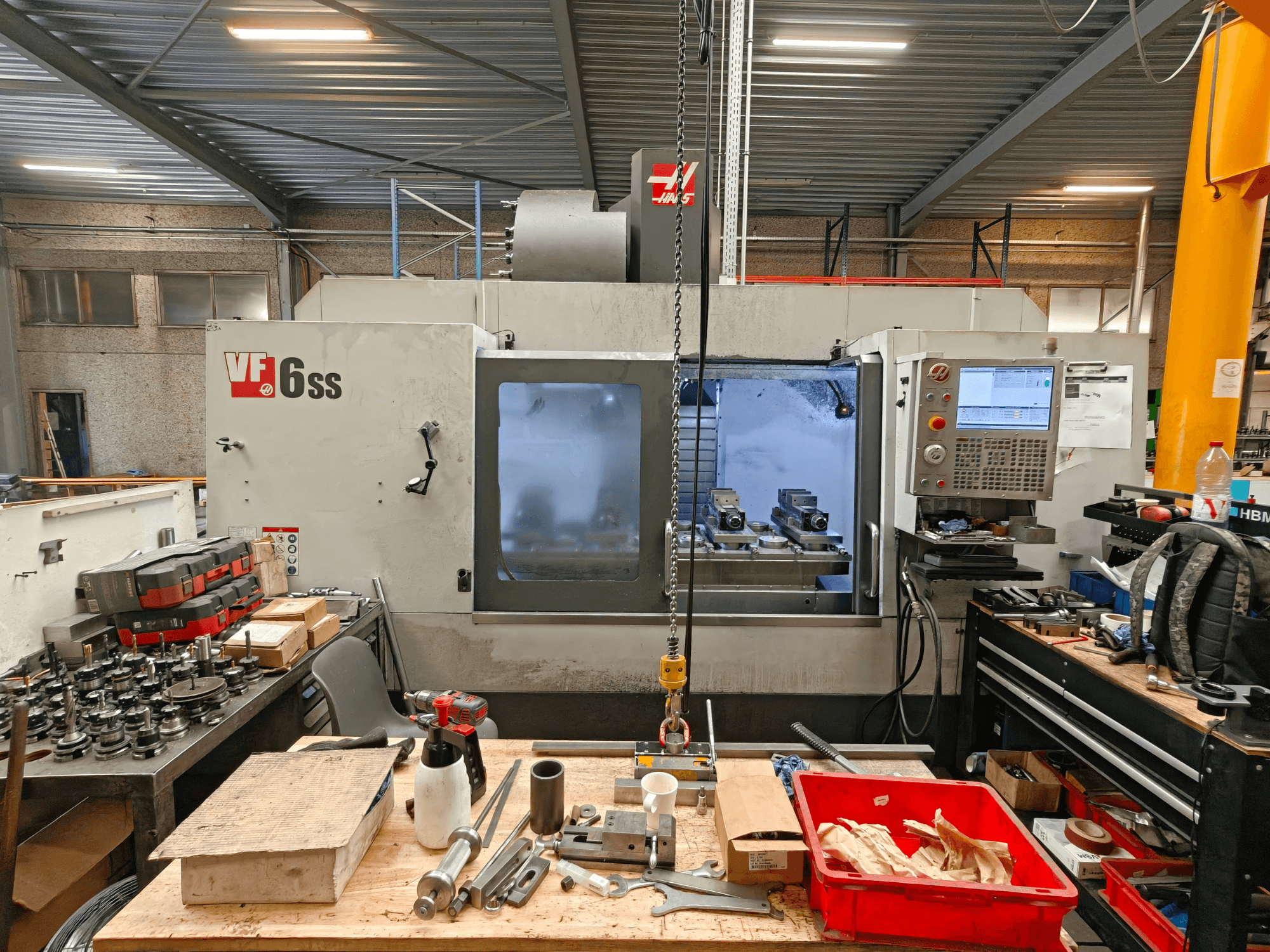 Pionowe centrum obróbcze Haas VF-6SS w warsztacie, widok z boku ukazujący panel sterowania oraz obszar roboczy zagracony narzędziami.
