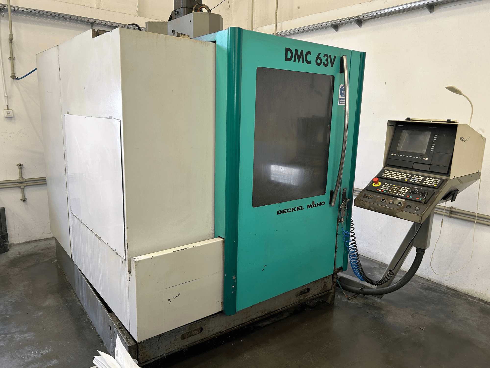 Pionowe centrum obróbcze DECKEL MAHO DMC 63V w widoku z przodu, z panelem sterowania i niebiesko-zieloną obudową.