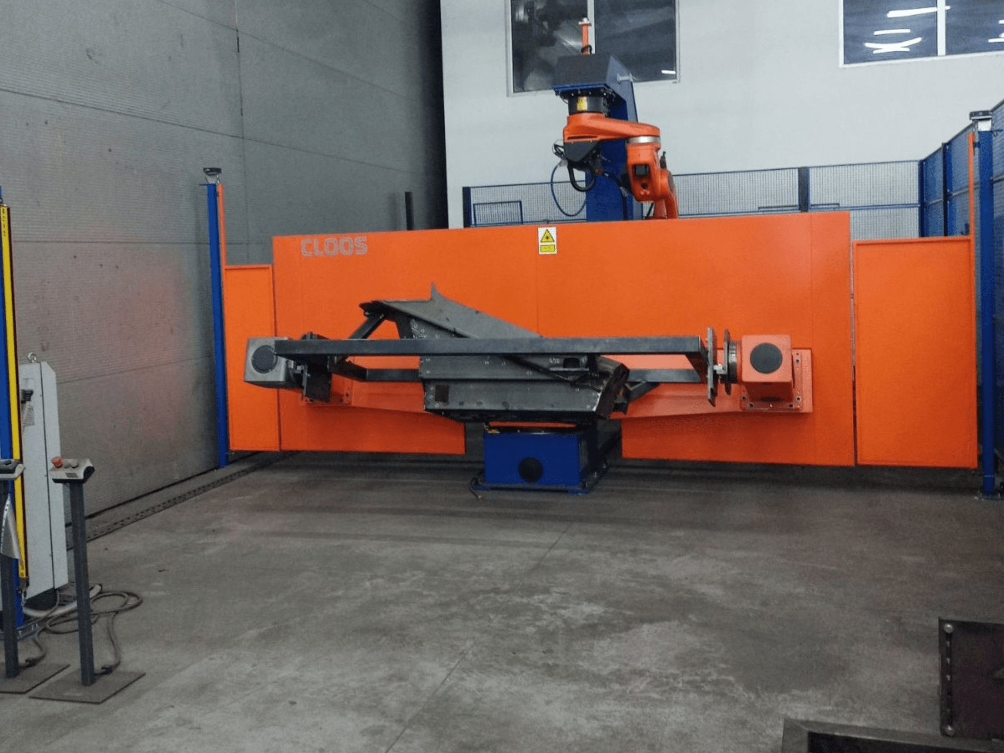 Widok z przodu systemu automatyki CLOOS QIROX QRC-350-E z ramieniem robota i konstrukcją metalową w środowisku przemysłowym.