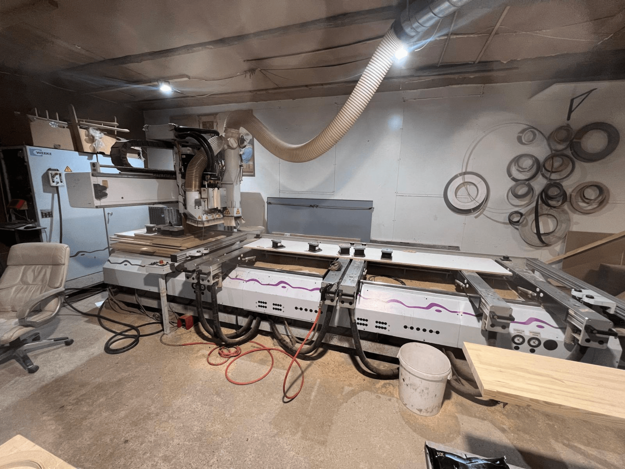 Centrum obróbki drewna CNC Weeke OPTIMAT BP 120 w warsztacie, widok z przodu, z widocznymi na blacie kawałkami drewna i narzędziami.