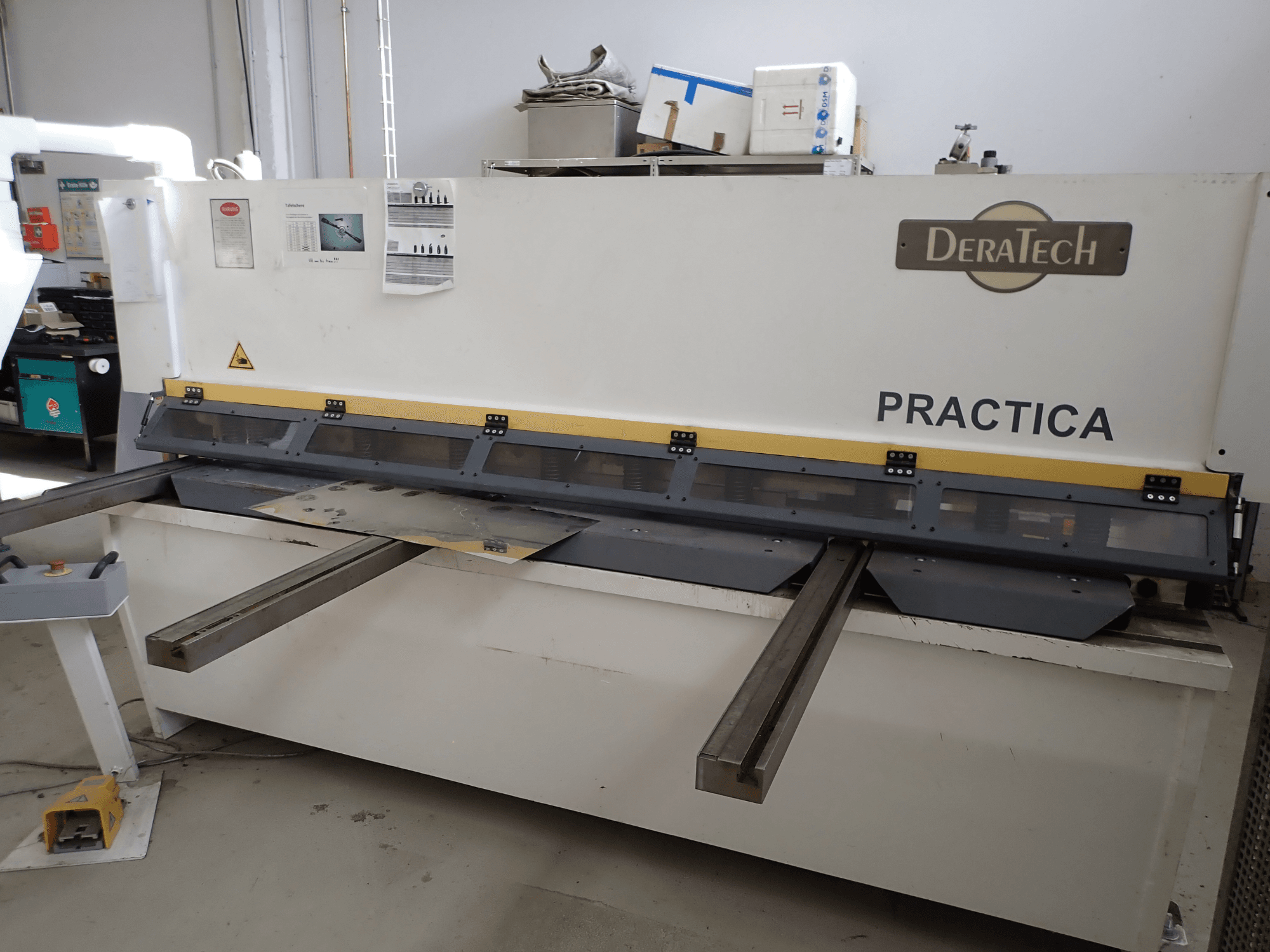 Nożyce CNC DERATECH Practica, widok z przodu, pokazujący ostrze tnące i blachy na powierzchni roboczej.