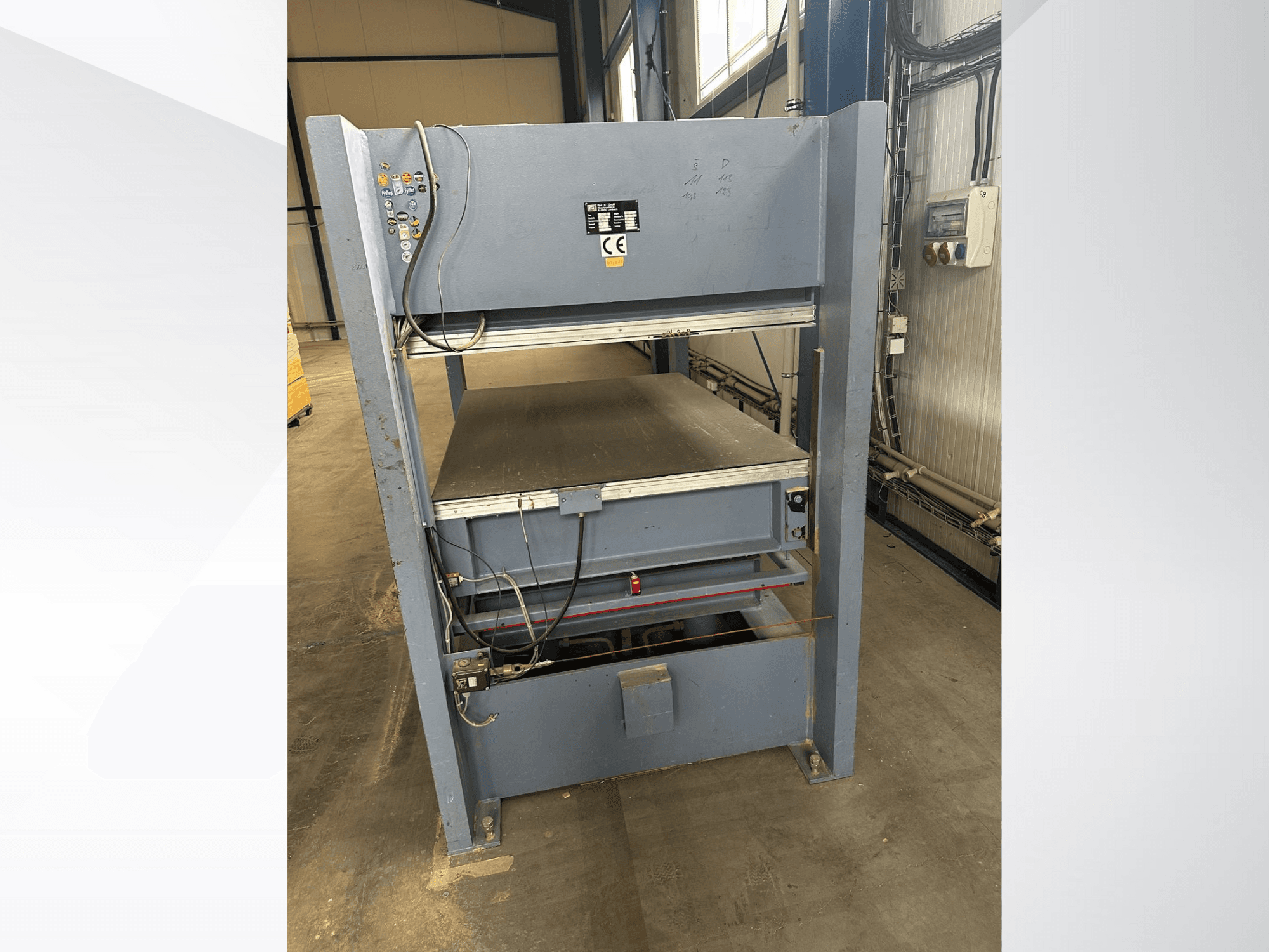 Szara maszyna przemysłowa z panelem sterowania, patrząc od przodu; zawiera regulowane platformy i oznaczenia bezpieczeństwa.