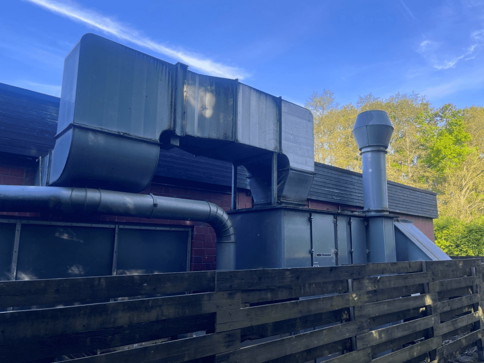 Przemysłowy system wentylacyjny z metalowymi kanałami, widok z boku; zawiera kwadratowy i cylindryczny komin, zielone wykończenie.