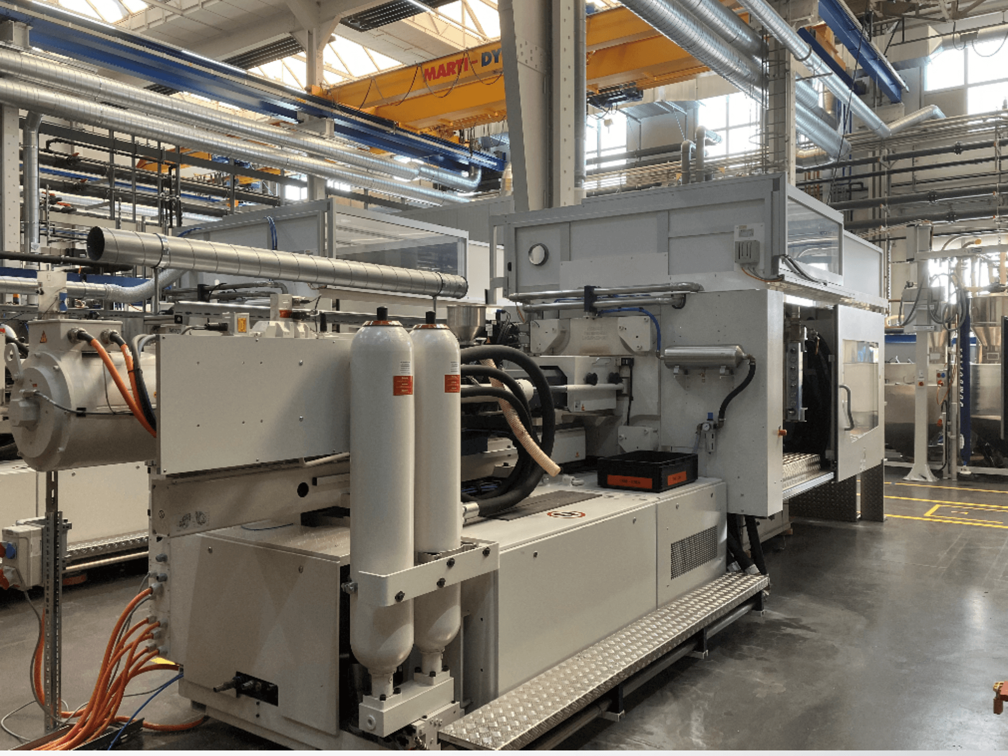 Maszyna przemysłowa pokazana w widoku z boku z wieloma wężami, dwoma pionowymi zbiornikami i panelem sterowania; marka/model niewidoczne.