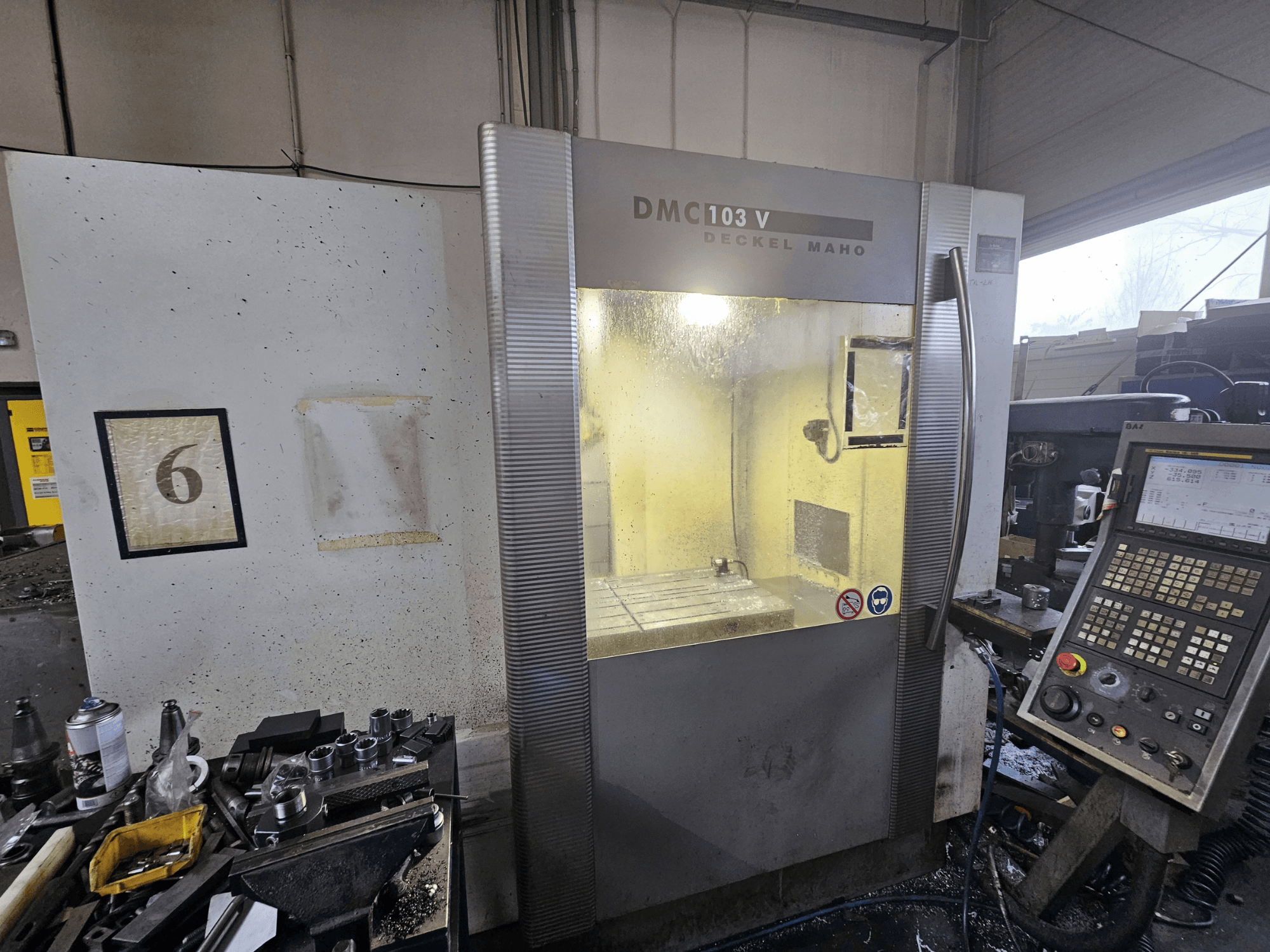 Widok z przodu maszyny CNC Deckel Maho DMC 103 V, pokazujący panel sterowania, obszar roboczy i numerowany wskaźnik "6".