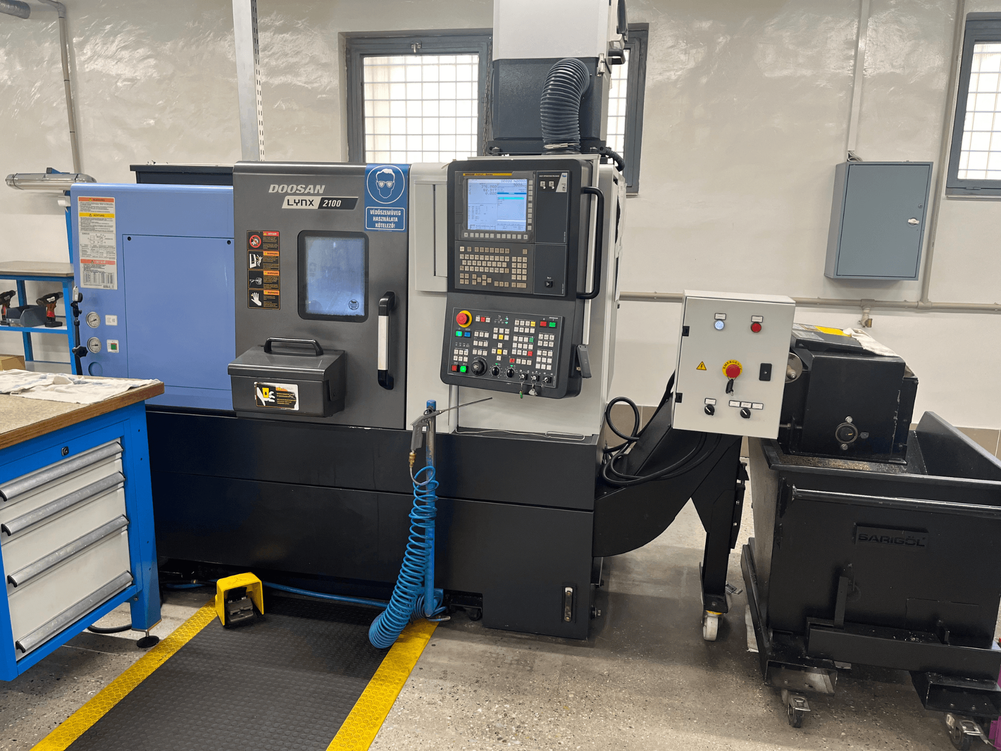 Tokarka Doosan Lynx 210 w warsztacie, pokazująca panel sterowania, magazyn narzędzi i układ chłodzenia, widok z boku ze szczegółami przestrzeni roboczej.