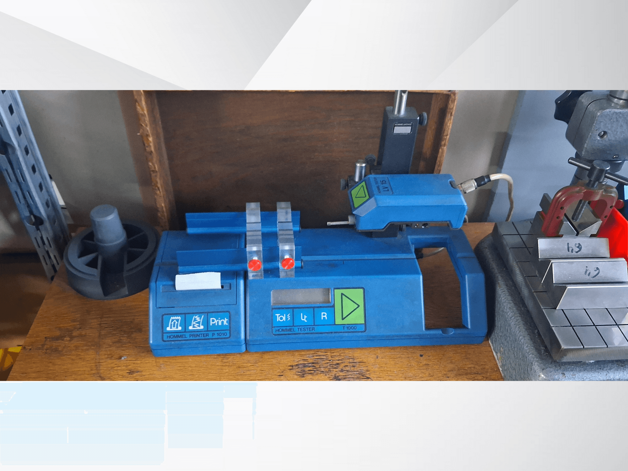 Niebieska drukarka Hommel T 1000 i tester T 1 010 z czerwonymi przyciskami, widziane od przodu na stole warsztatowym z metalowymi blokami.