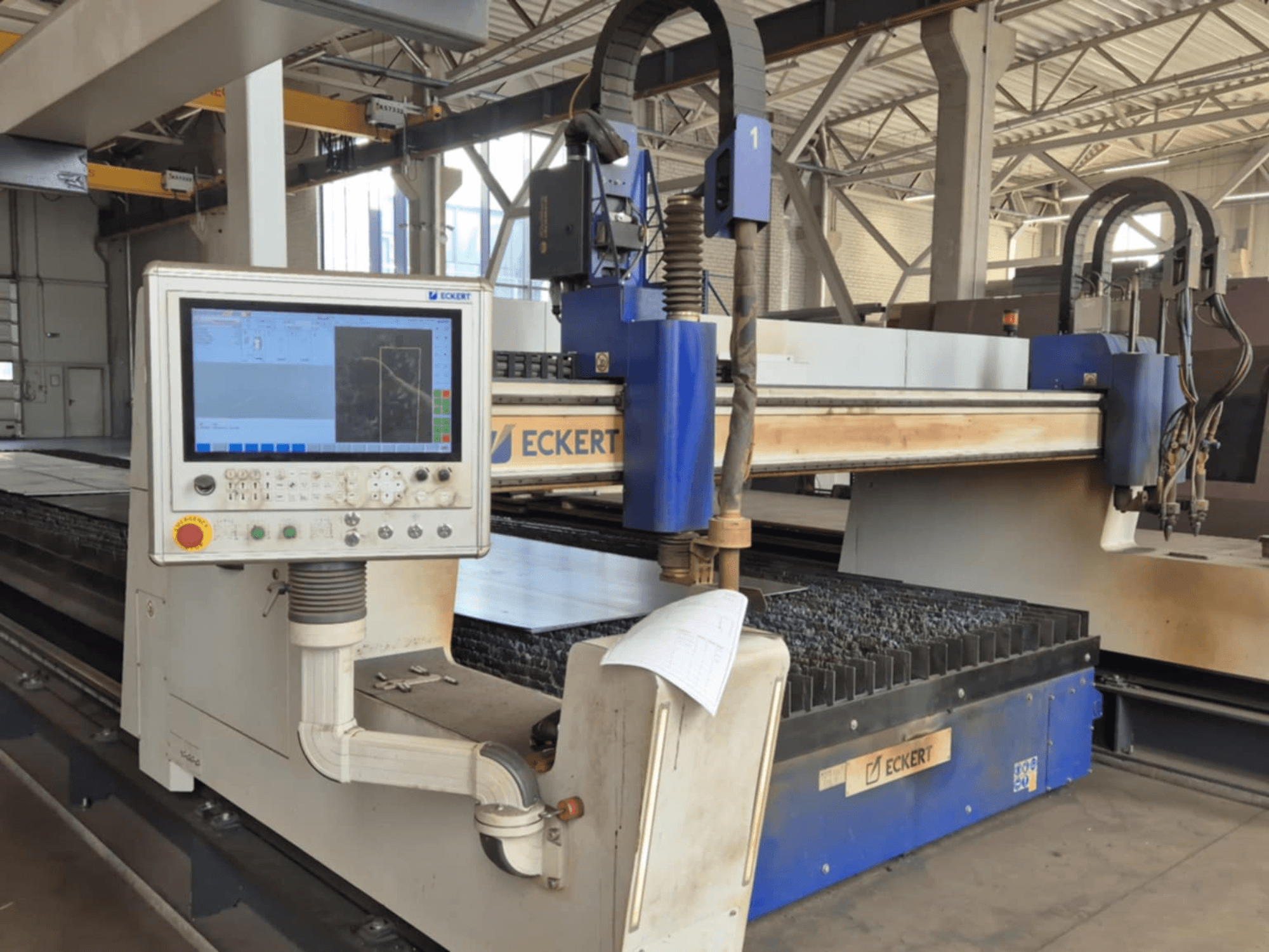 Panel sterowania maszyny do cięcia CNC firmy ECKERT w widoku z przodu, z ekranem dotykowym i różnymi przyciskami operacyjnymi.