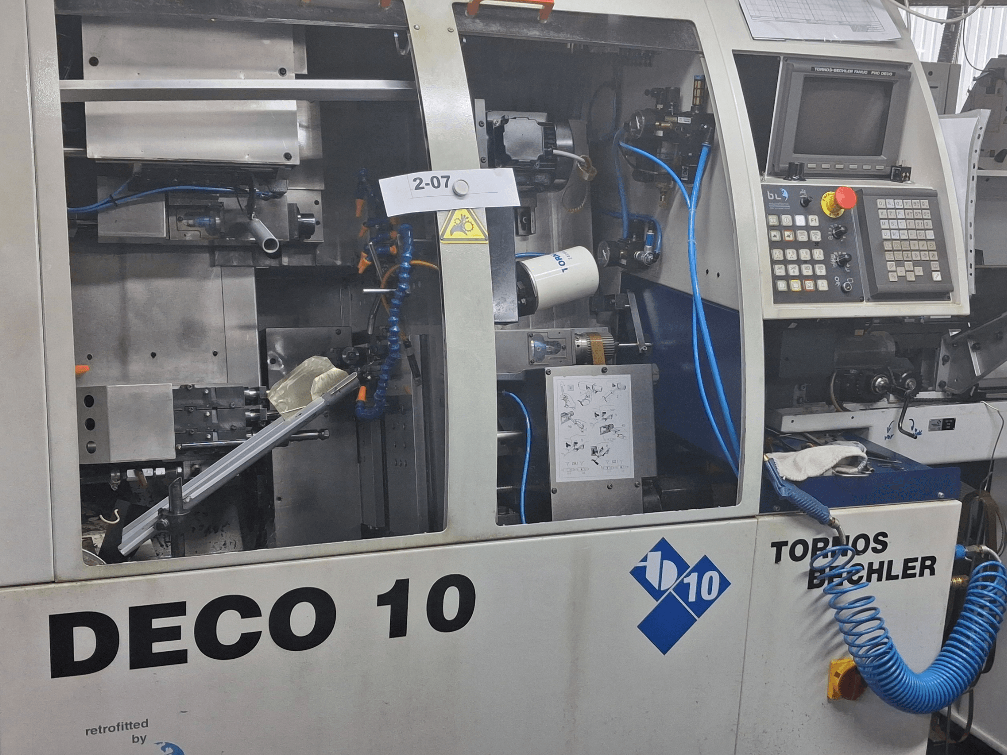 Widok z bliska tokarki TORNOS Deco 10a typu szwajcarskiego, przedstawiający wewnętrzny mechanizm i szczegóły panelu sterowania.