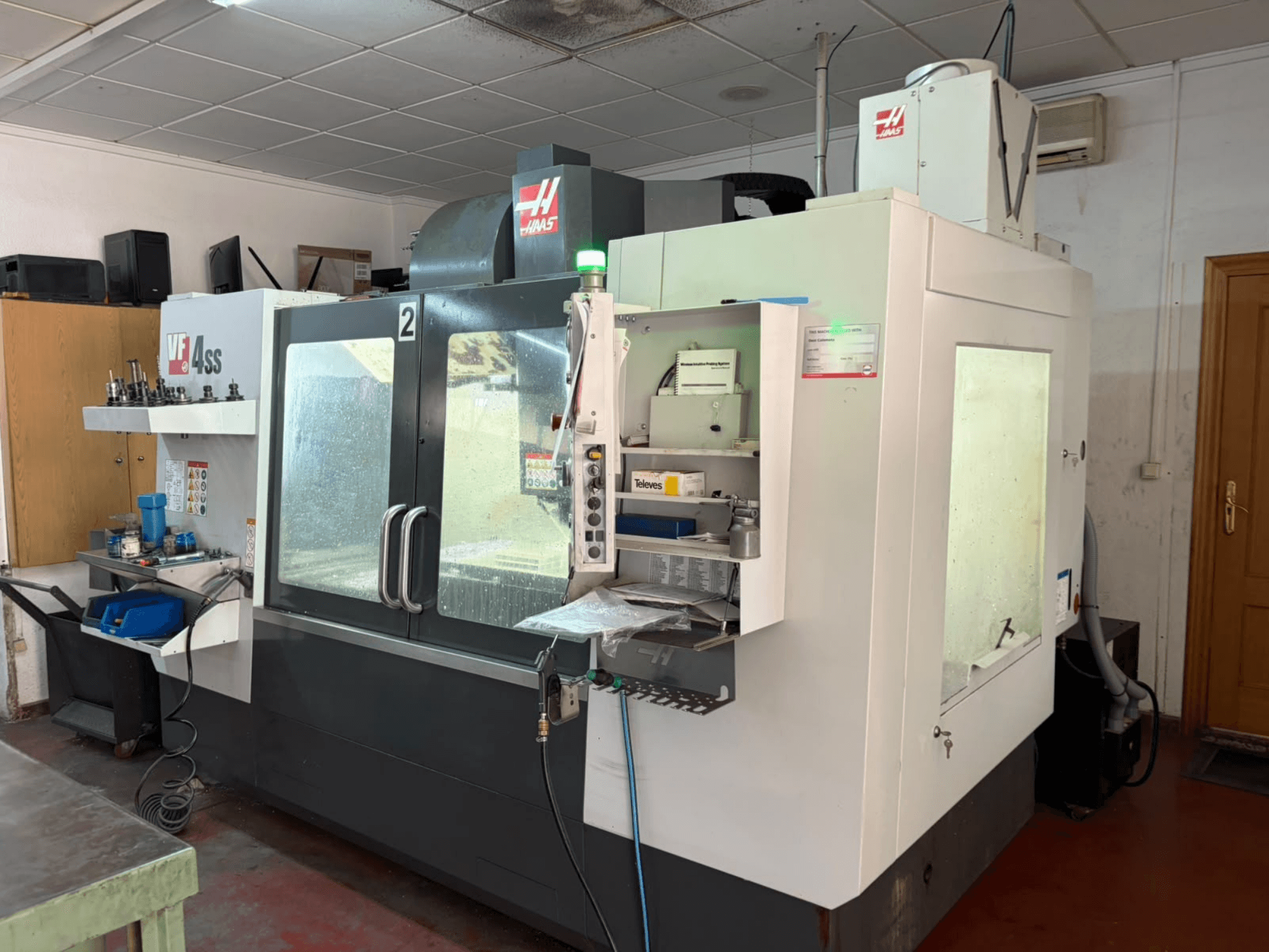 Pionowe centrum obróbcze HAAS VF 4SS w warsztacie, widok z przodu, przedstawiający panel sterowania oraz obszar roboczy z narzędziami i materiałami.