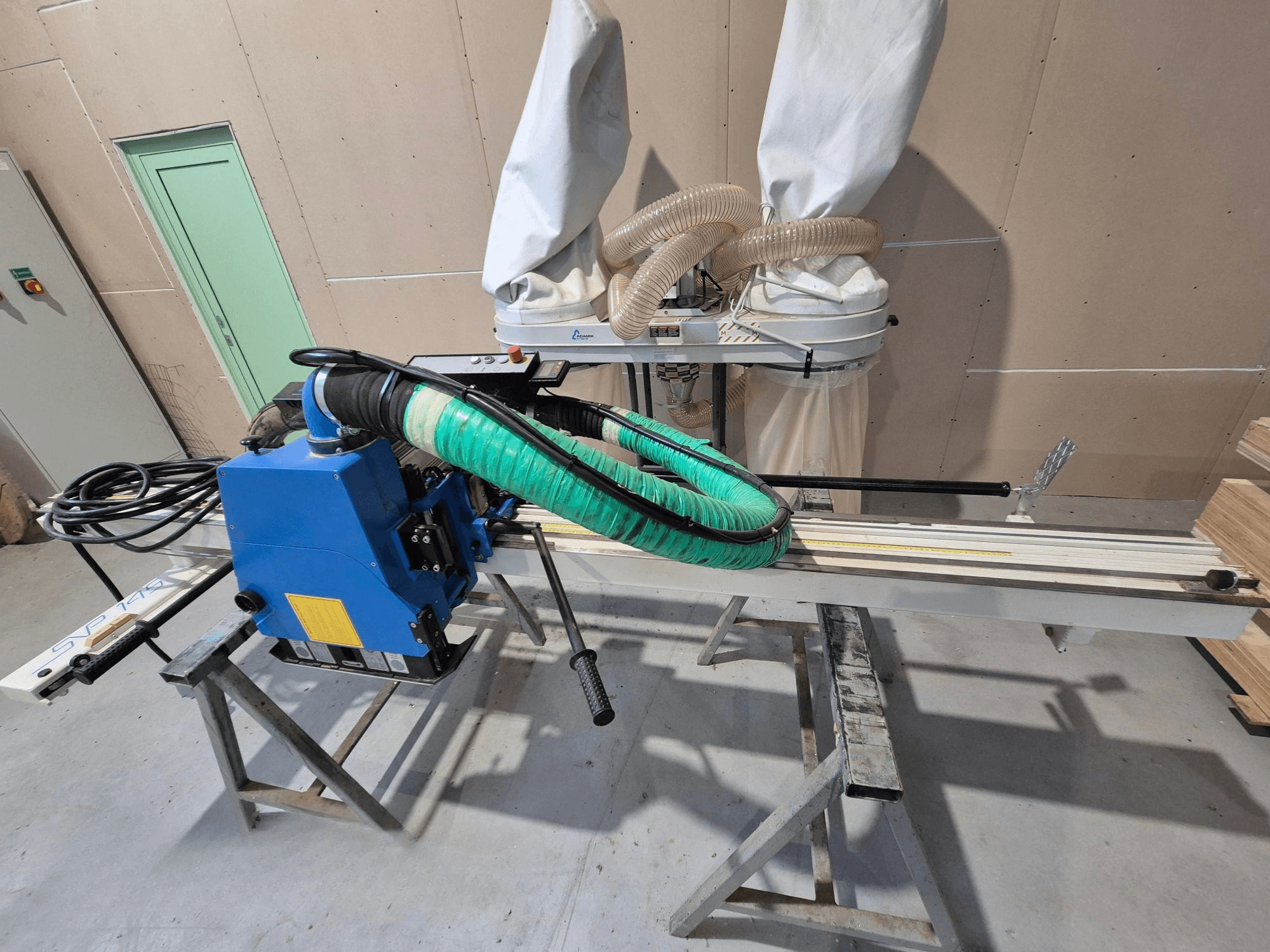 Niebieska pozioma pilarka panelowa SVP-175 z zielonym wężem pyłowym i wspornikiem, widziana z boku w warunkach warsztatowych.