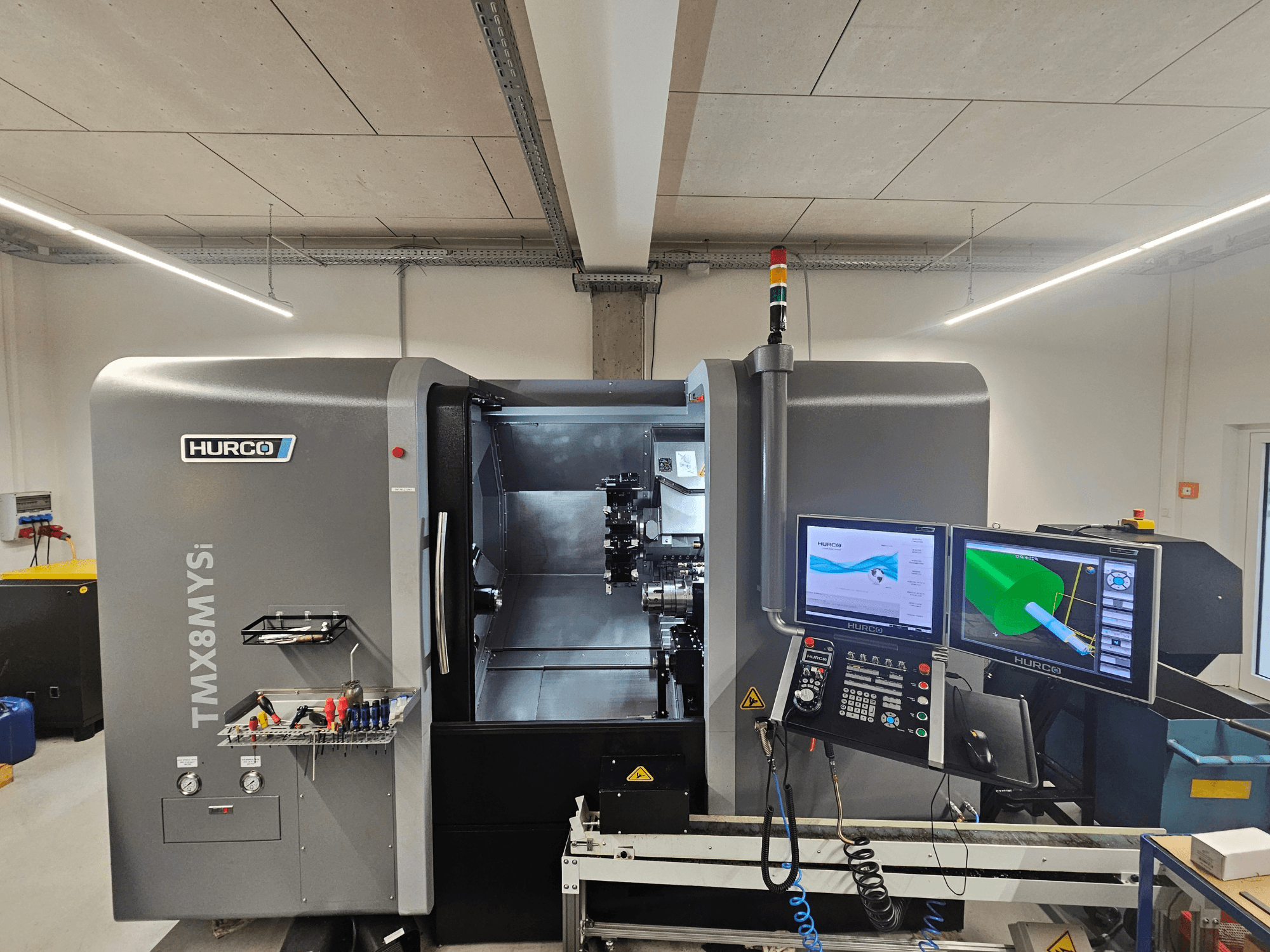 Centrum frezarskie Hurco TMX 8 MYSi w warsztacie, z dwoma monitorami, panelem sterowania i narzędziami z boku.