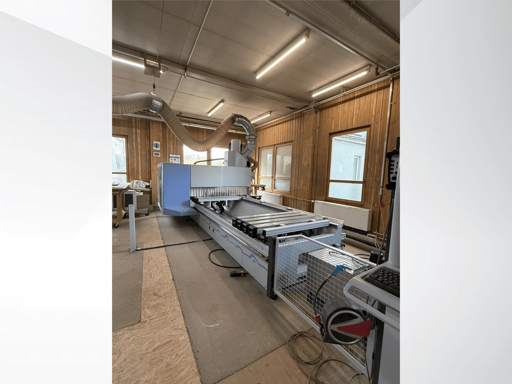 Frezarka CNC w warsztacie, widok z boku, z dużym niebieskim korpusem, dołączonym przenośnikiem taśmowym i widocznym panelem sterowania.