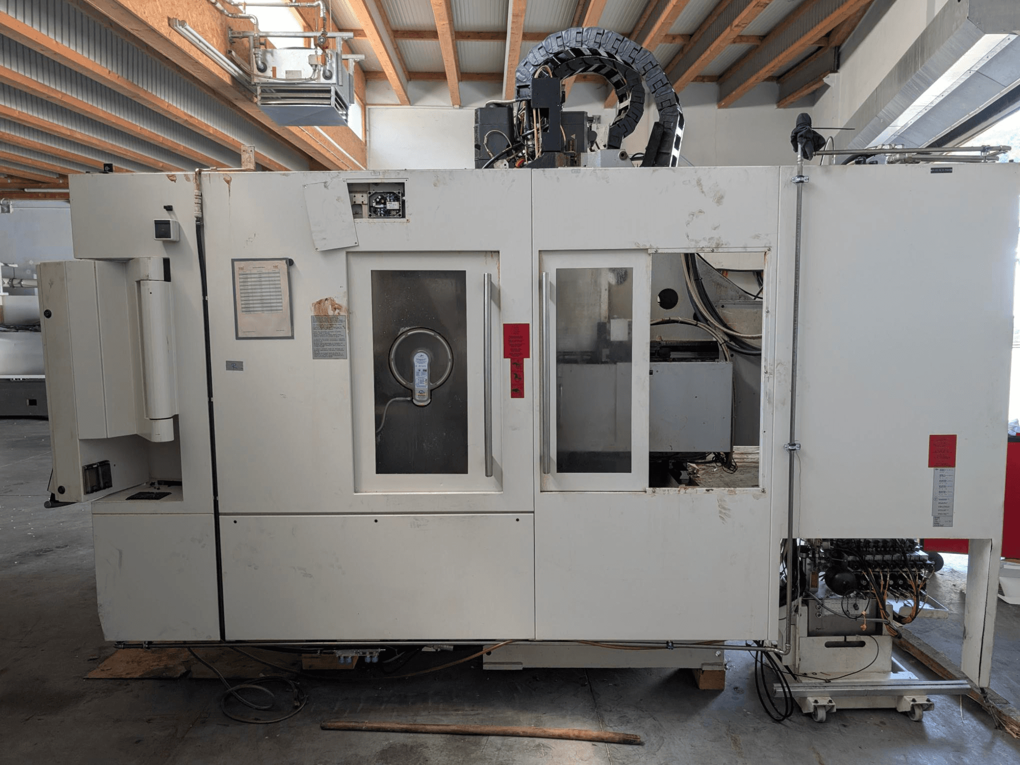 Pionowe centrum obróbcze STAMA MC 326, widok z boku pokazujący panel sterowania, obszar wrzeciona i różne etykiety na maszynie.