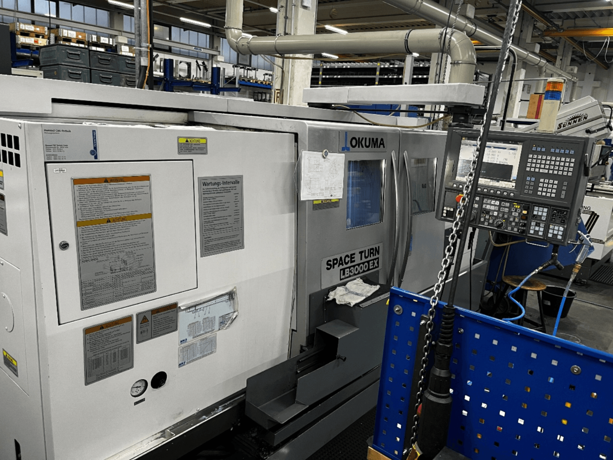 Obracarka pozioma Okuma LB3000 EX, widok z przodu, panel sterowania i informacje dotyczące bezpieczeństwa z boku.