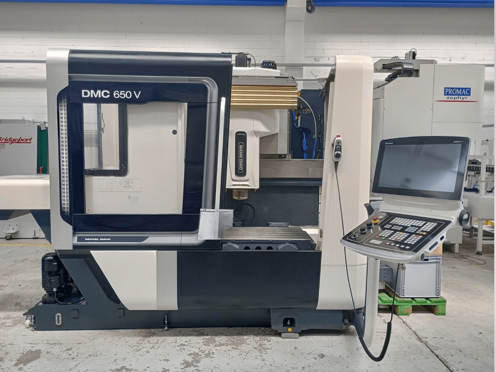 Widok z boku maszyny Decker Maho DMC 650 V CNC, z panelem sterowania z przyciskami i ekranem, w otoczeniu przemysłowym.