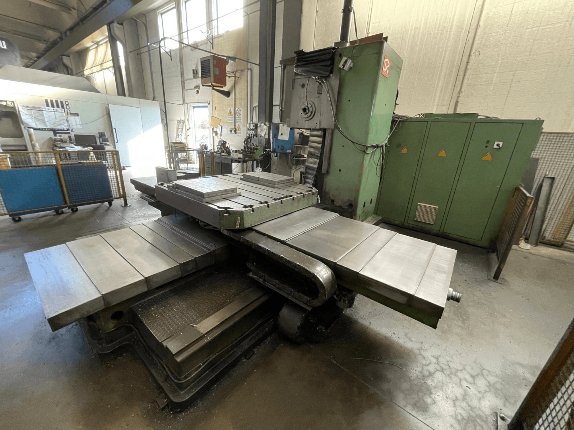 Duża frezarka przemysłowa z zielonym korpusem, widok z boku, z wieloma płaskimi powierzchniami i szafkami do przechowywania w tle.