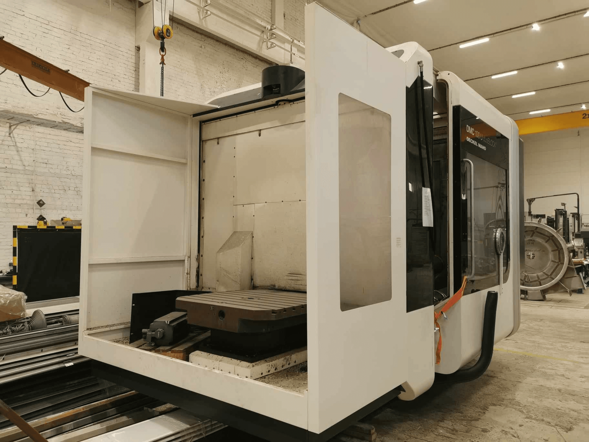 Liniowa maszyna CNC DMC 100U, widok z boku z otwartymi drzwiami dostępowymi, pokazujący stół roboczy i elementy wewnętrzne.
