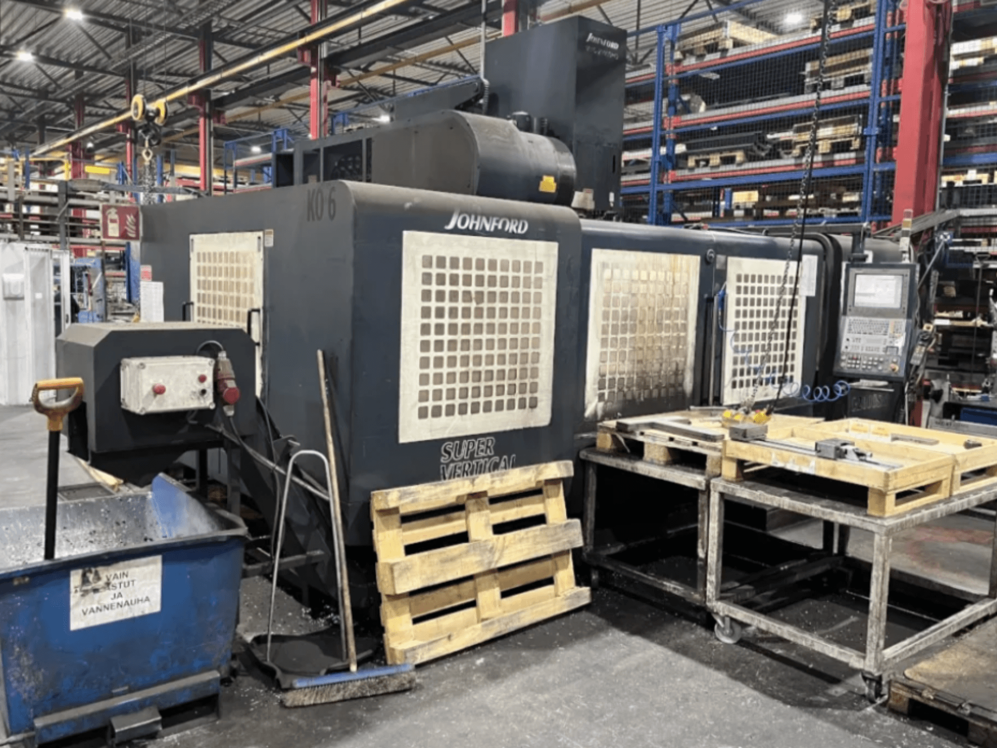 Frezarka Johnford Super Vertical w fabryce, widok z boku z panelem sterowania, paletami i sprzętem czyszczącym w pobliżu.