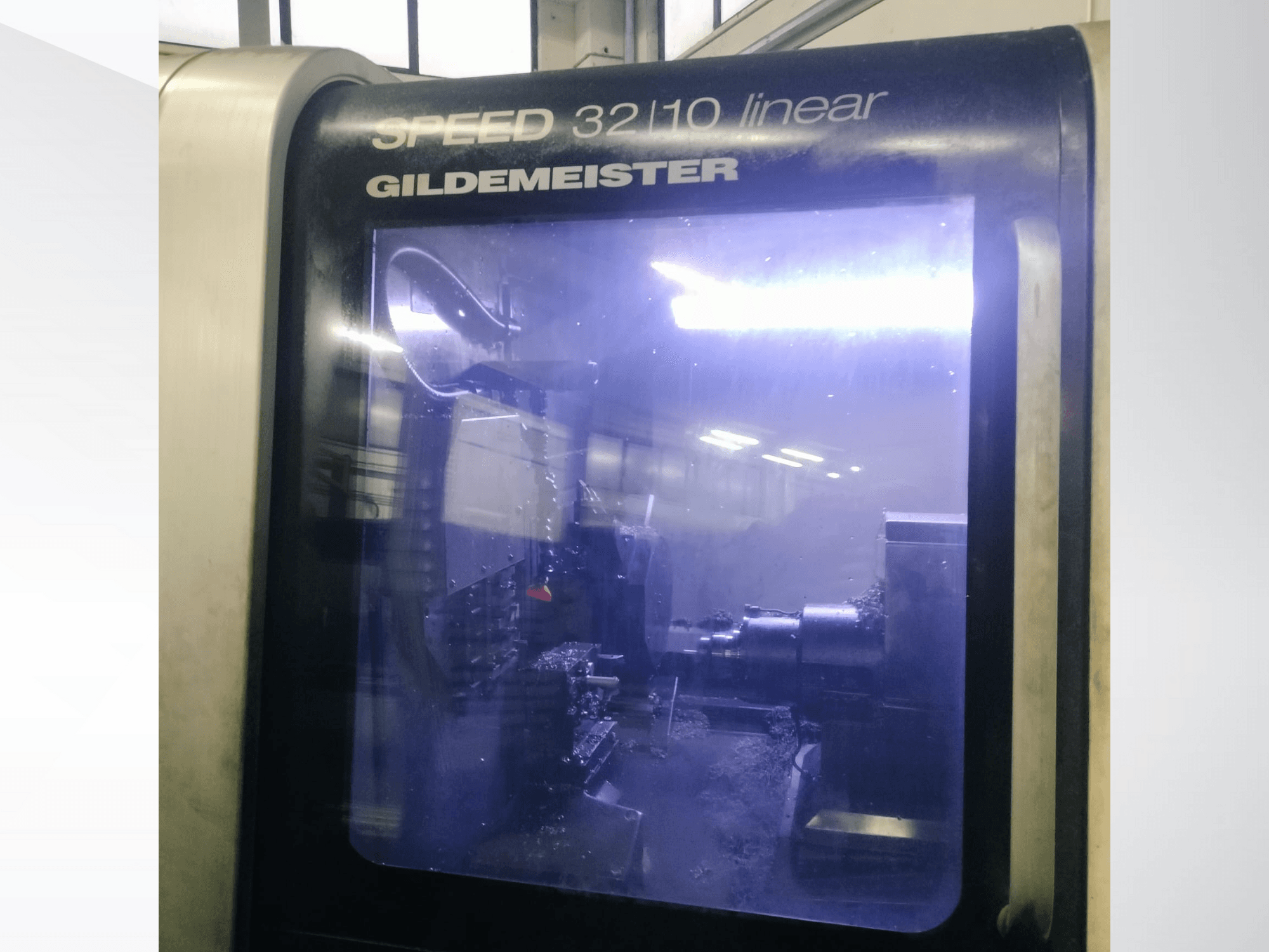 Liniowa maszyna CNC Gildemeister SPEED 3210 widok z przodu, pokazujący wewnętrzne komponenty i ciecz chłodzącą podczas pracy.
