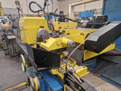 Żółta maszyna przemysłowa z czarną sekcją, tarczą i wężami, widziana z przodu pod niewielkim kątem.