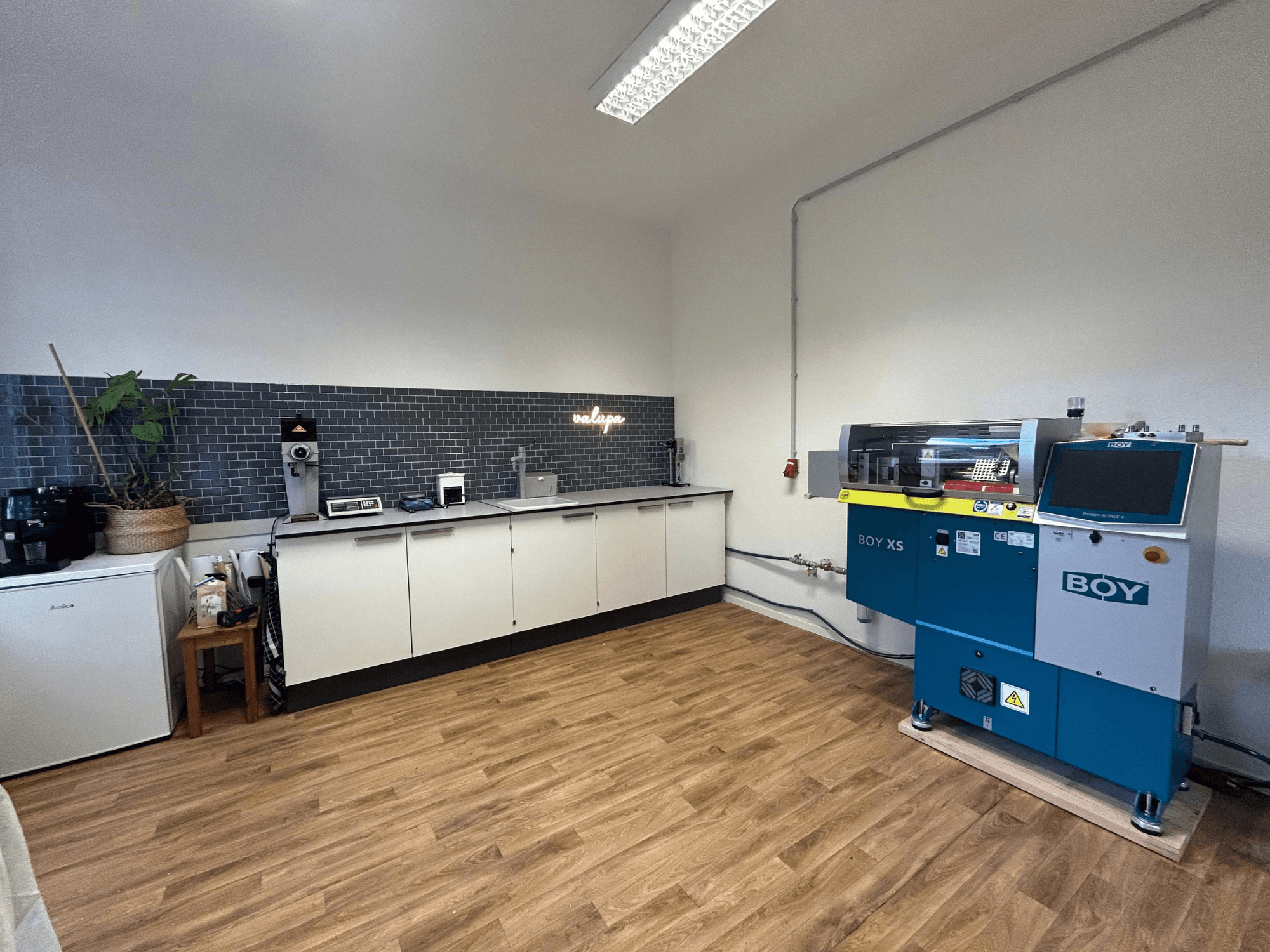 Hydrauliczna wtryskarka BOY XS 161, widok z przodu, w nowoczesnej kuchni z urządzeniami i drewnianą podłogą.