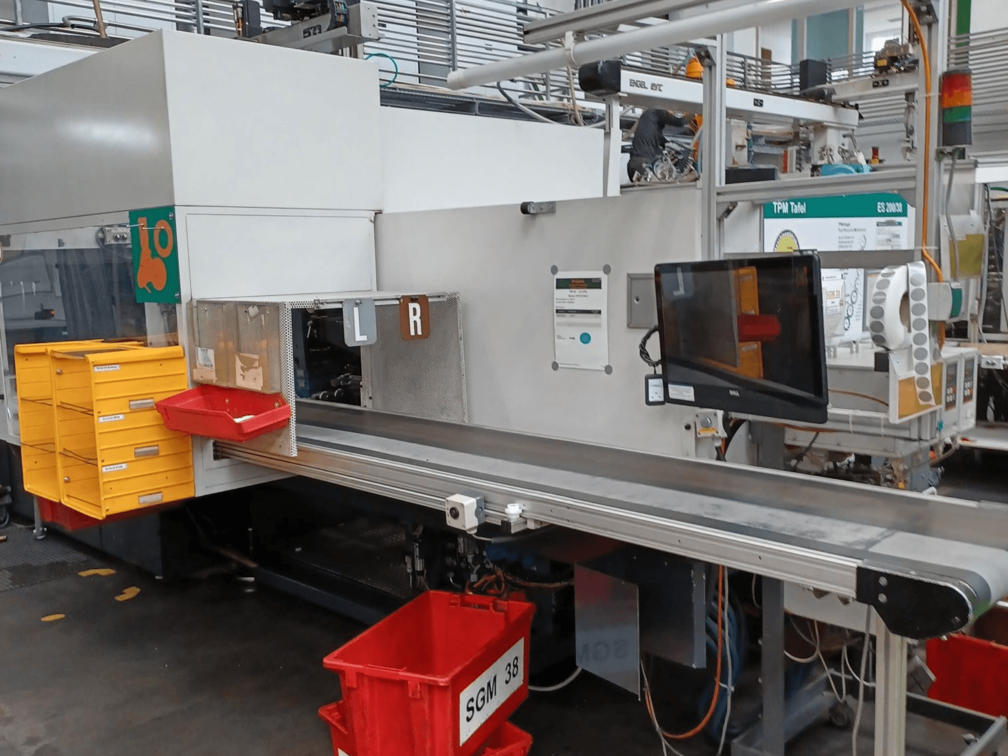 Przemysłowa maszyna sortująca z żółtymi i czerwonymi pojemnikami, widok z boku, wyposażona w monitor kontrolny i oznaczone przedziały do sortowania.