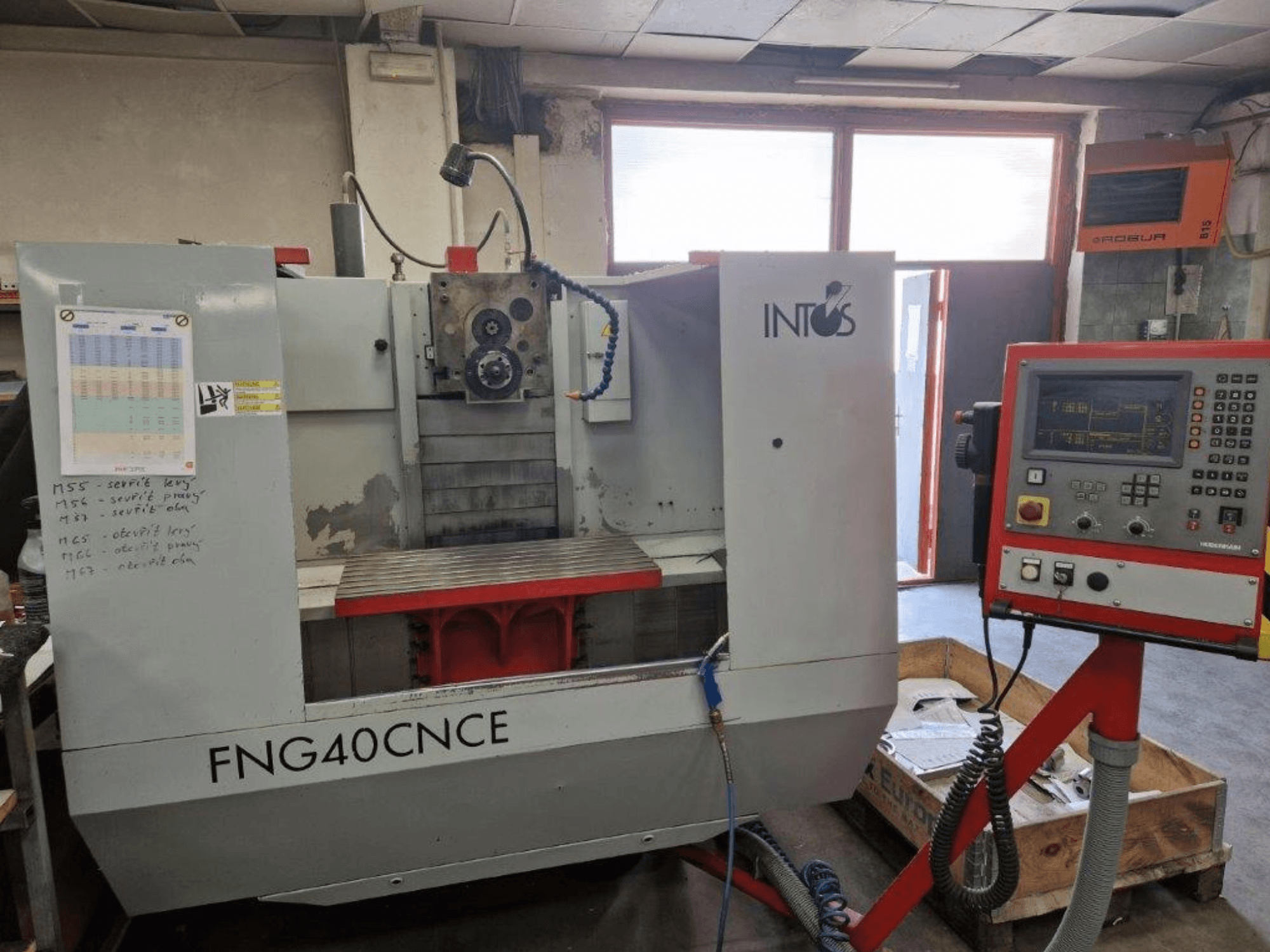 Maszyna INTOS FNG40CNC, widok z przodu, posiada panel sterowania, części operacyjne i metalowy stół roboczy. Idealna do obróbki skrawaniem.