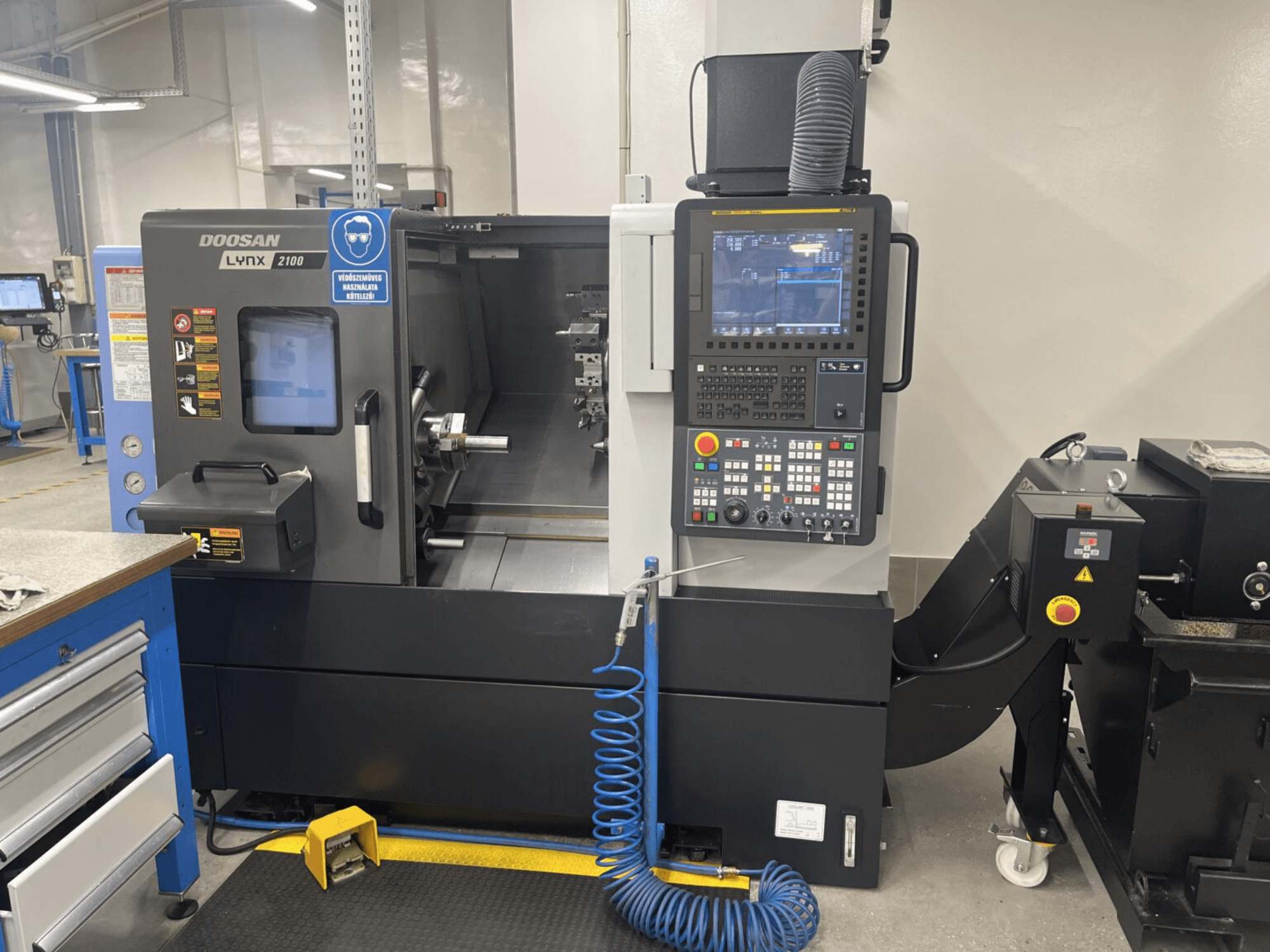 Widok z przodu tokarki poziomej DOOSAN Lynx 2100A, przedstawiający panel sterowania i obszar wrzeciona z ważnymi funkcjami bezpieczeństwa.
