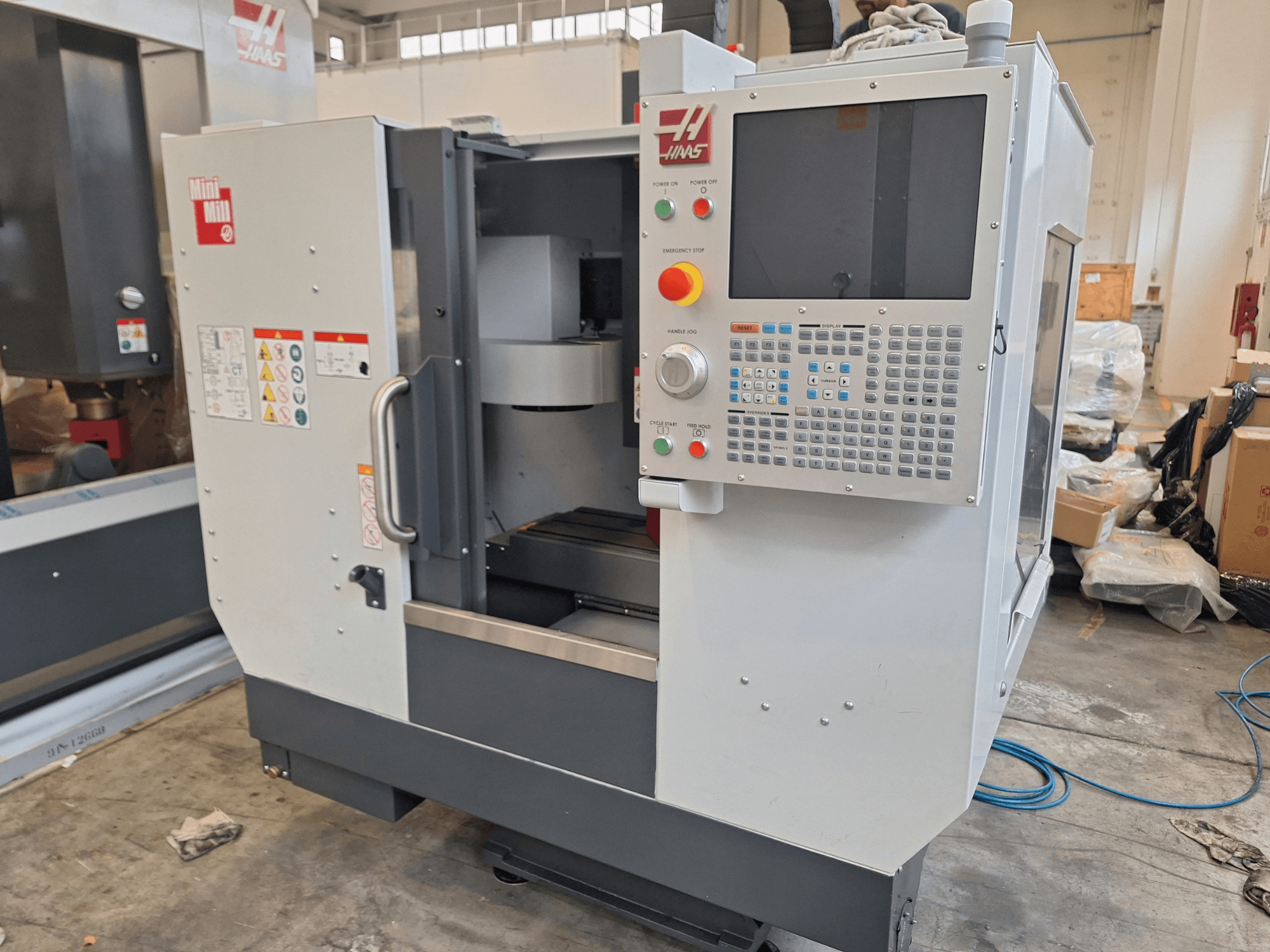 Pionowe centrum obróbcze HAAS Mini Mill widziane z przodu, wyposażone w panel sterowania z przyciskami i ekranem wyświetlacza.