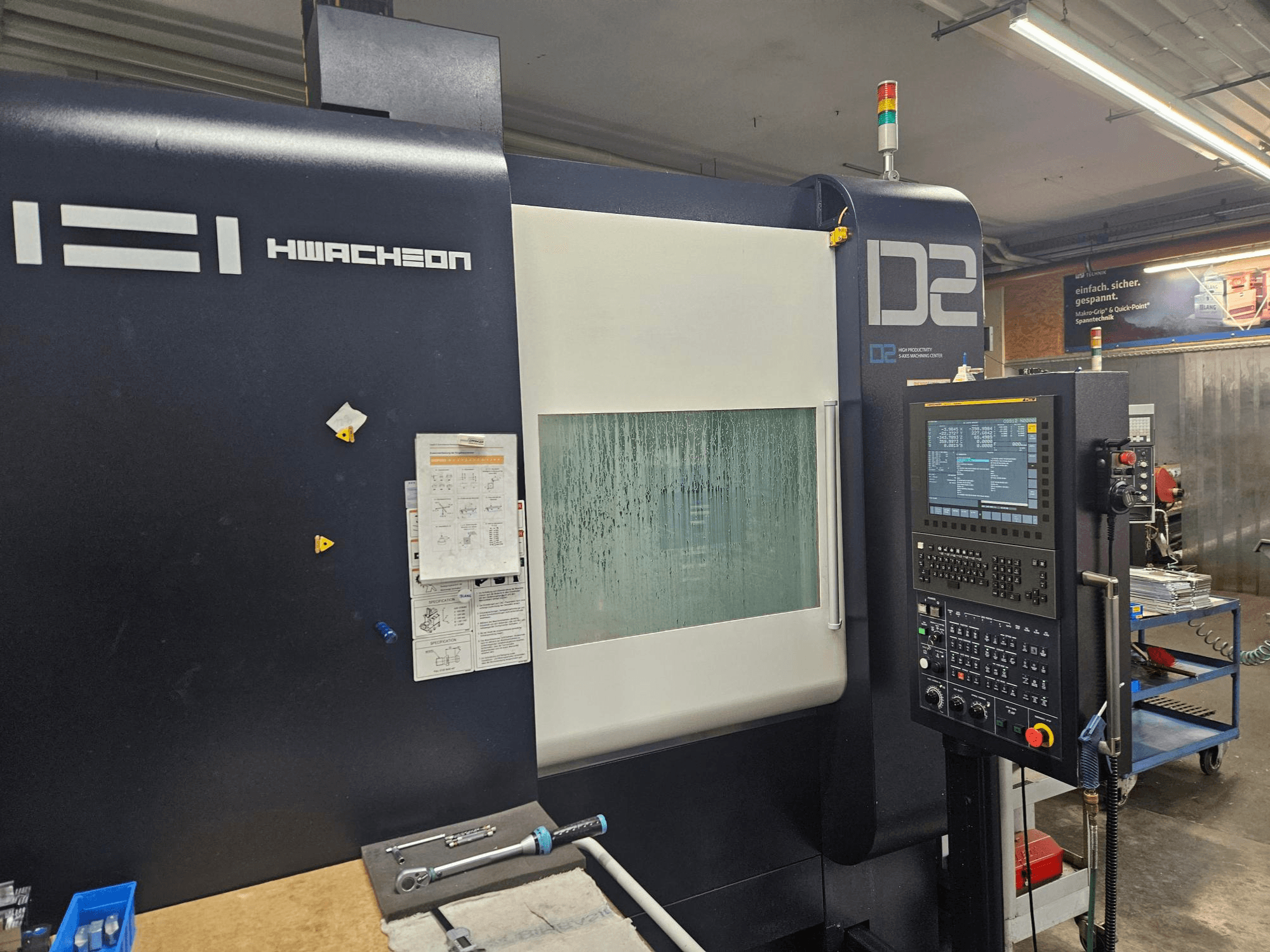 Centrum obróbcze HWACHEON D2-5AX 12k z pionowym układem obróbki, widok z przodu przedstawiający panel sterowania i zaparowane okienko podglądowe.