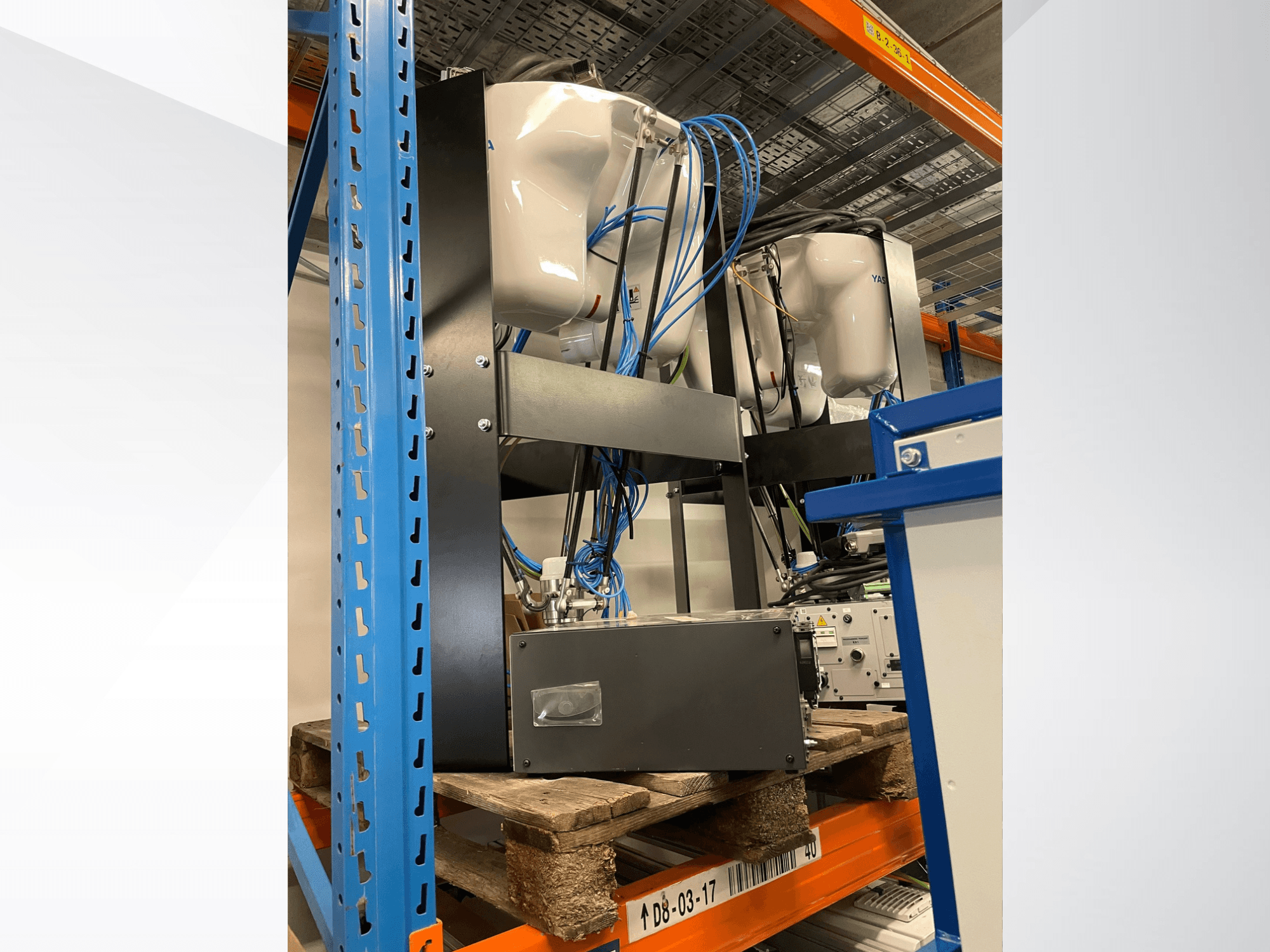 Ramię robota Yaskawa Motoman MPP3H, widok z boku, z widocznymi przewodami i komponentami na regale magazynowym.