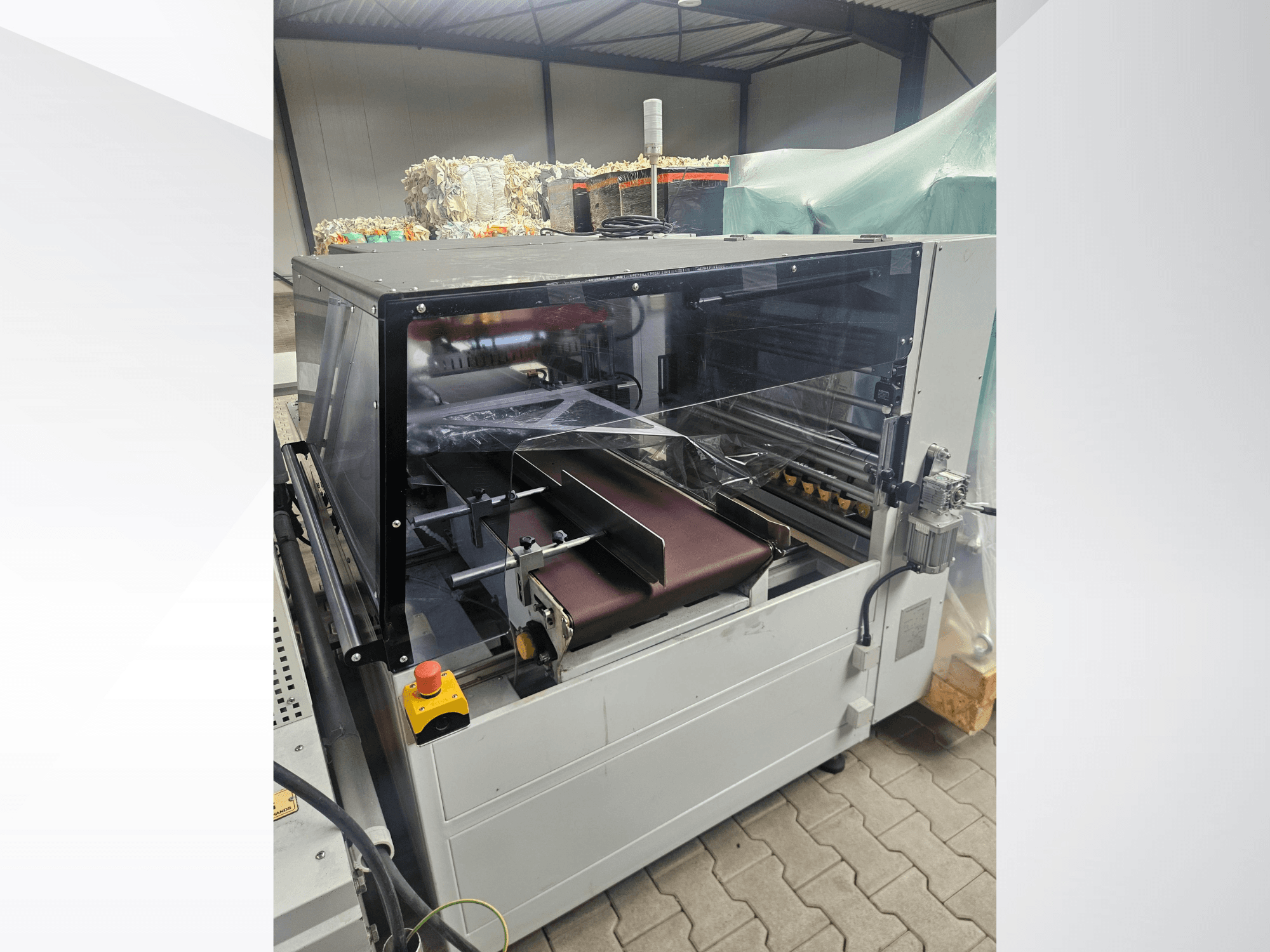 Maszyna AMTEC Speed Shrink 40 PRO, widok z przodu, przedstawiająca mechanizm do przetwarzania tworzyw sztucznych z przezroczystą osłoną zabezpieczającą i taśmą przenośnikową.