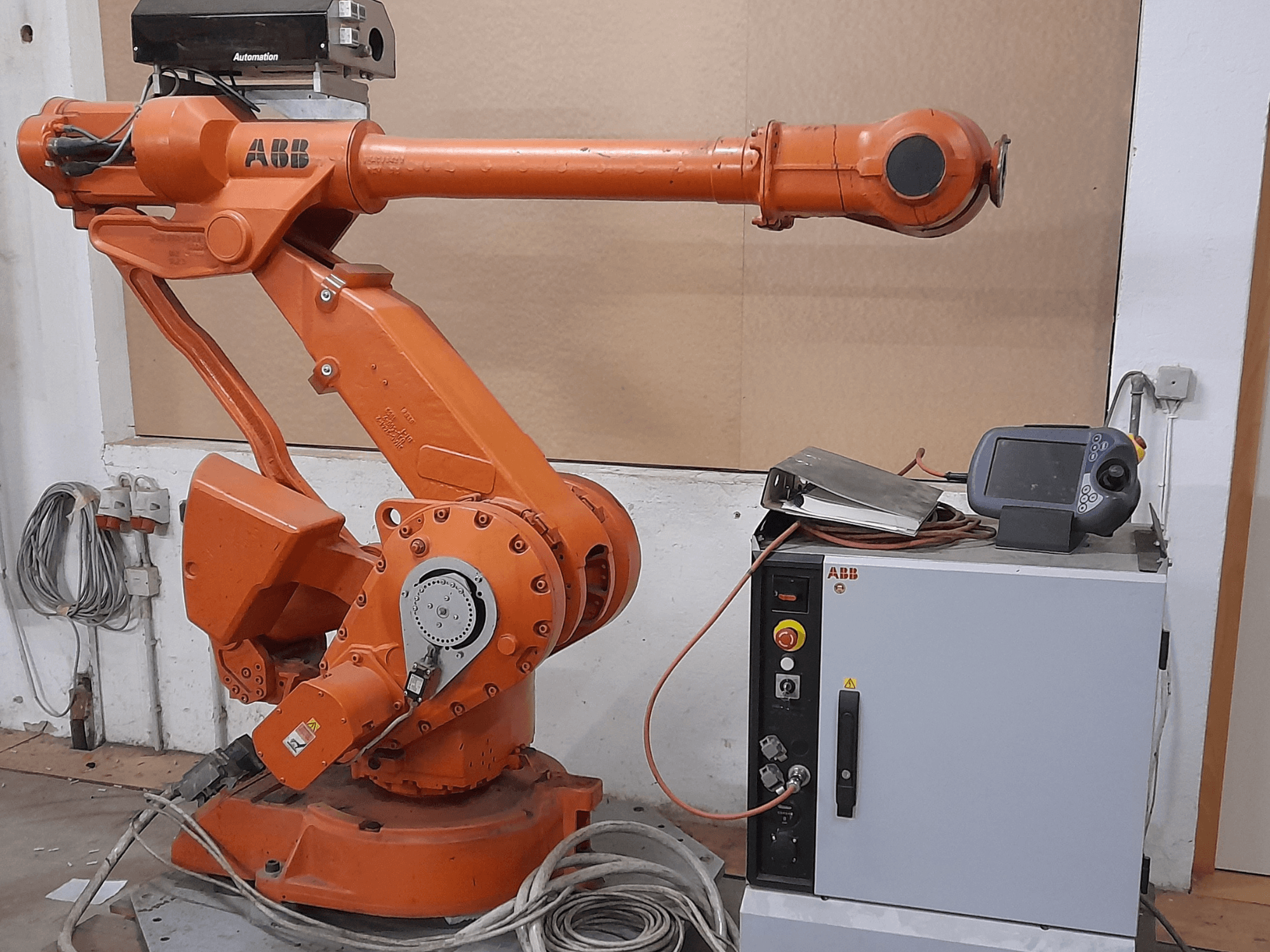 Pomarańczowe ramię robotyczne ABB z panelem sterowania, widok z przodu, pokazujące kable i sprzęt automatyki.