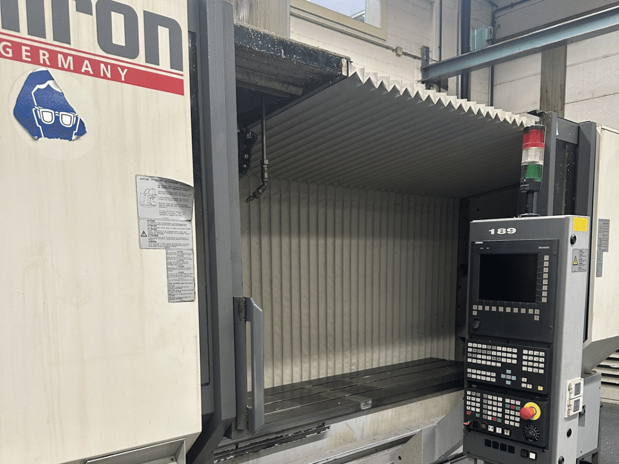 Alt text: Widok z przodu maszyny CNC Hermle z panelem sterowania z przyciskami i wyświetlaczem, z otwartym obszarem roboczym.