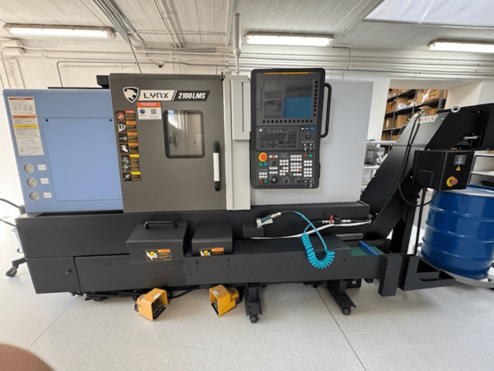 Tokarka pozioma DOOSAN LYNX 2100LMSA, widok z przodu, z panelem sterowania, wężem chłodziwa i schowkami.