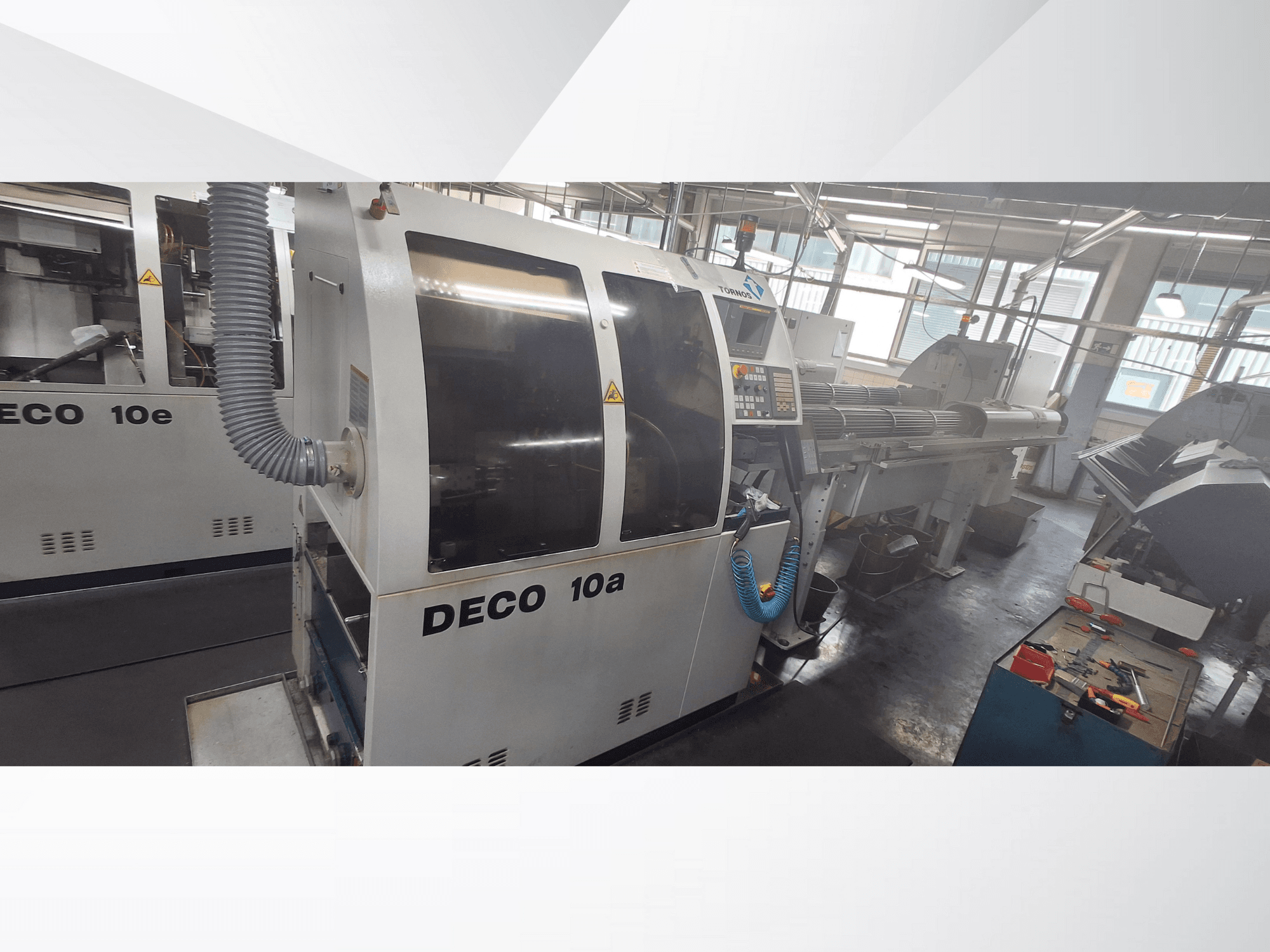 Maszyna CNC DECO 10a w warsztacie, widok z przodu, panel sterowania i układ wydechowy. Charakteryzuje się solidną konstrukcją i precyzyjnymi narzędziami.