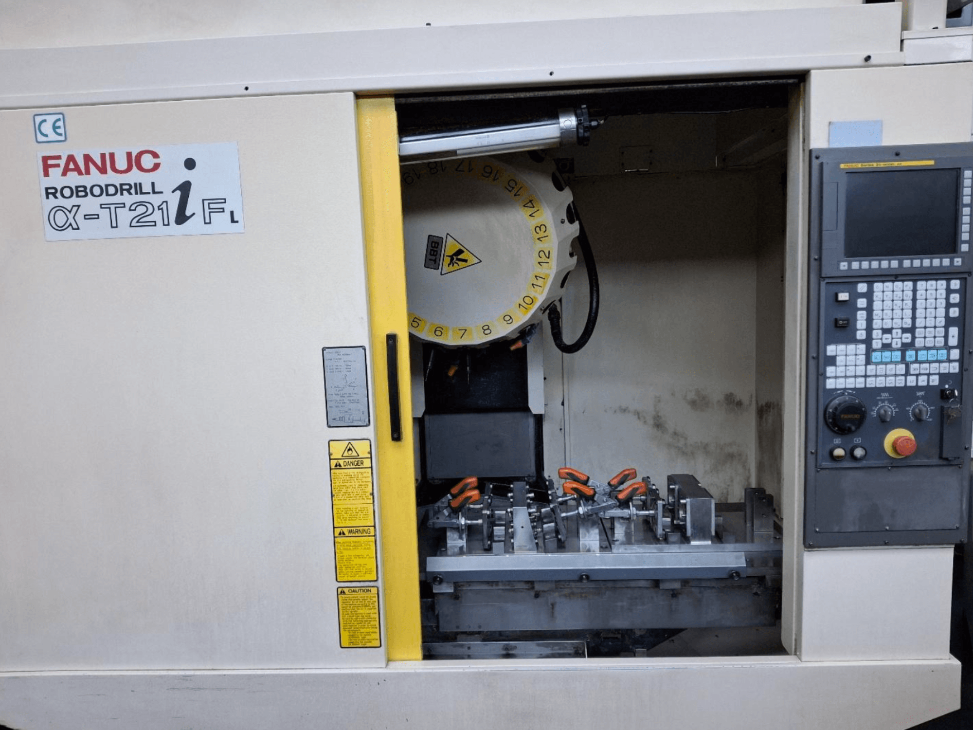 Widok z przodu pionowego centrum obróbczego FANUC ROBODRILL α-T21iFL, pokazujący narzędzia i elementy sterujące wewnątrz obudowy maszyny.